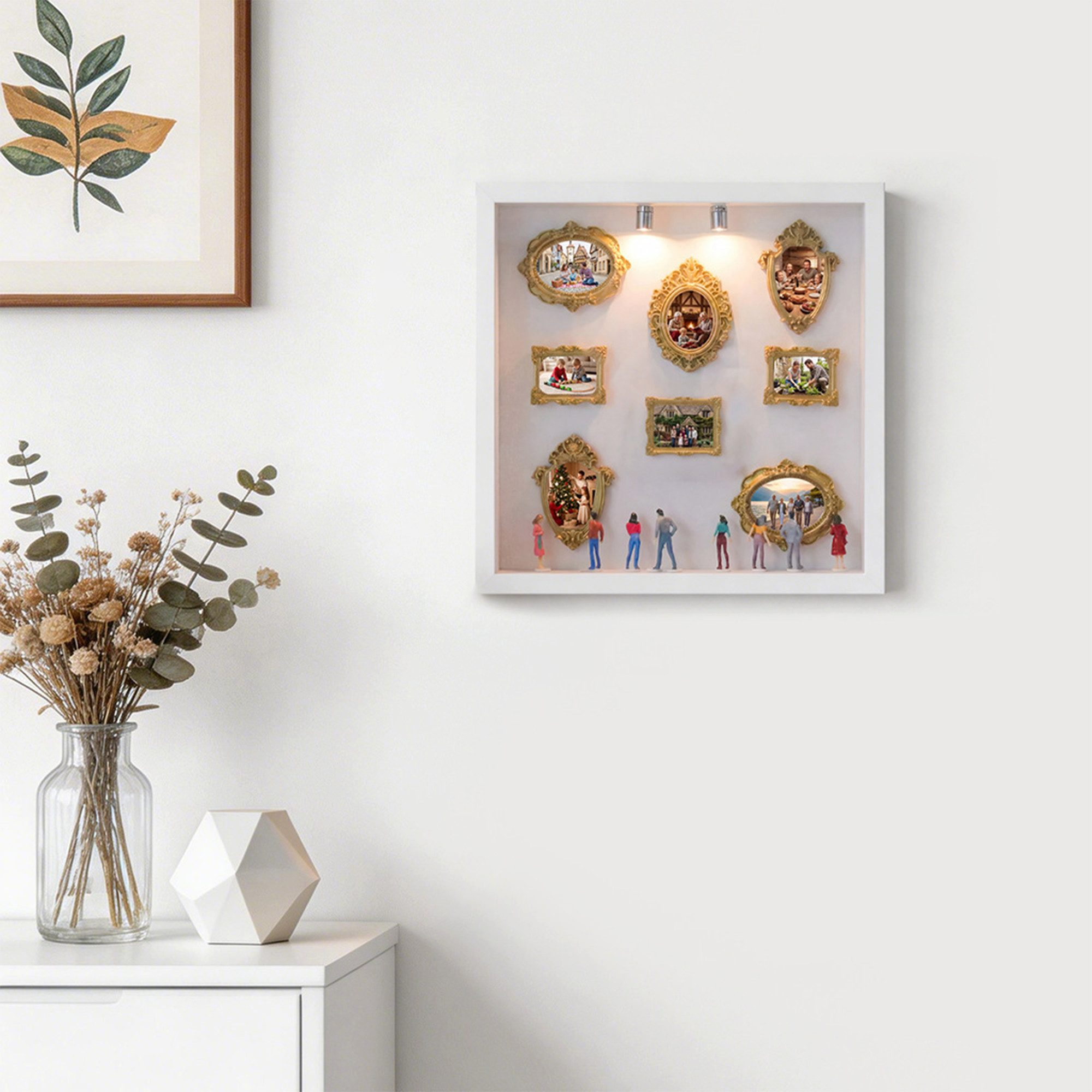 Beleuchteter weißer Kasten an der Wand mit antiken Fotorahmen und kleinen Menschenfiguren davor.