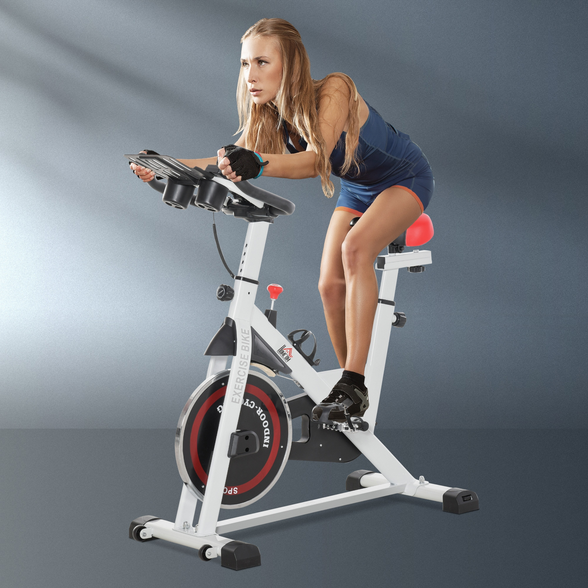 Una donna bionda in abbigliamento sportivo si allena su una cyclette bianca su sfondo grigio.