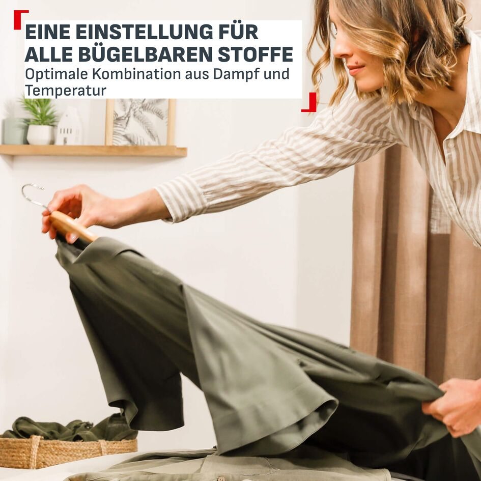 Eine Frau in gestreifter Bluse hält einen grünen Stoff an einem Kleiderbügel.