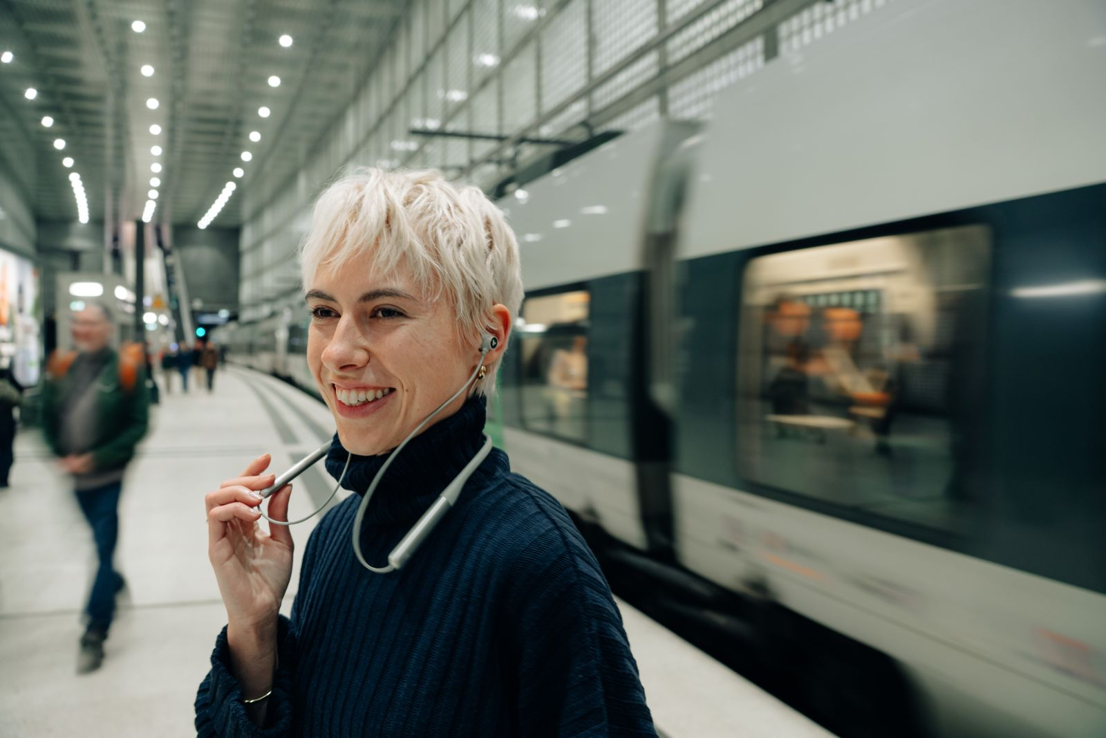 Una mujer rubia sonríe en el andén mientras llega un tren.