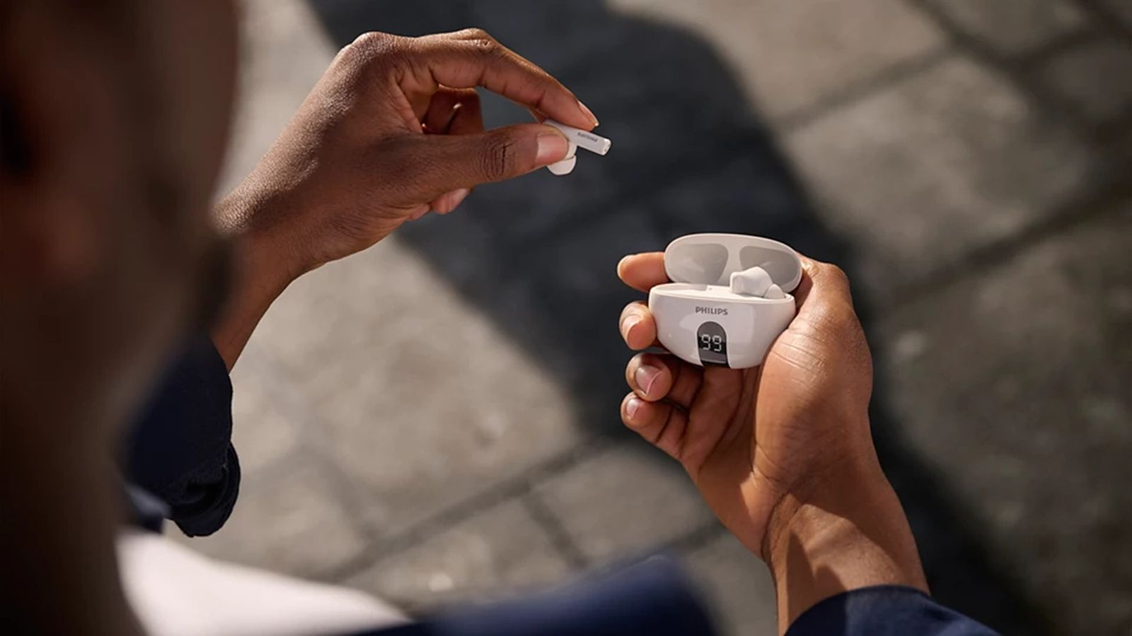 Person nimmt weiße Philips In-Ear-Kopfhörer aus dem Ladecase mit Digitalanzeige.