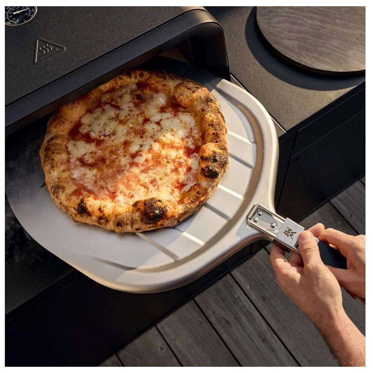 Una mano infila una pizza nel forno usando una pala.