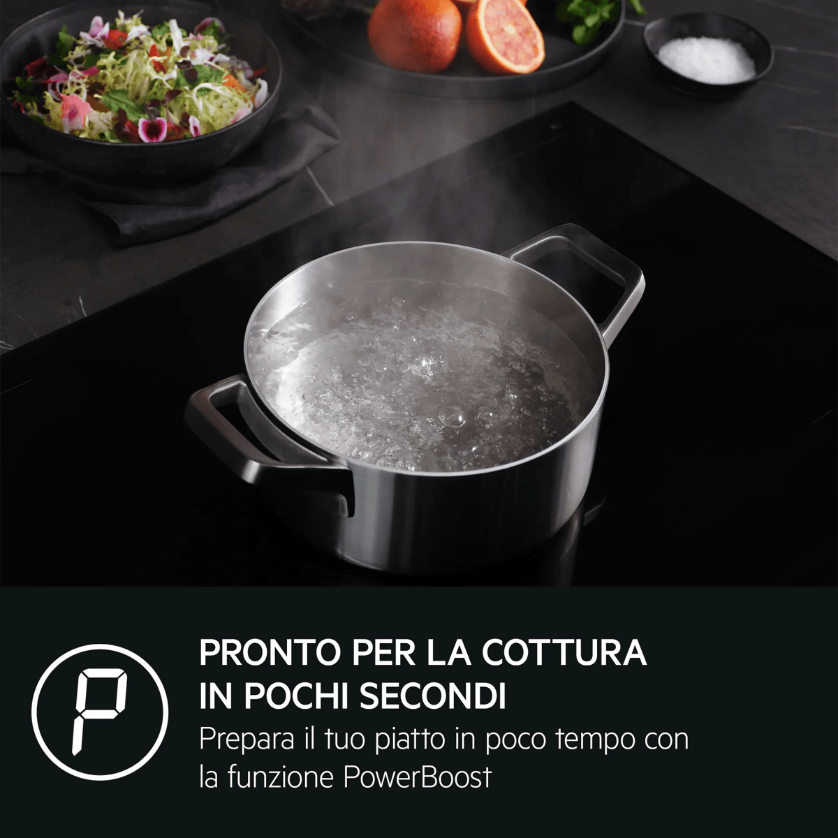 Acqua che bolle in una pentola d'acciaio su piano a induzione, con insalata e arance sullo sfondo.