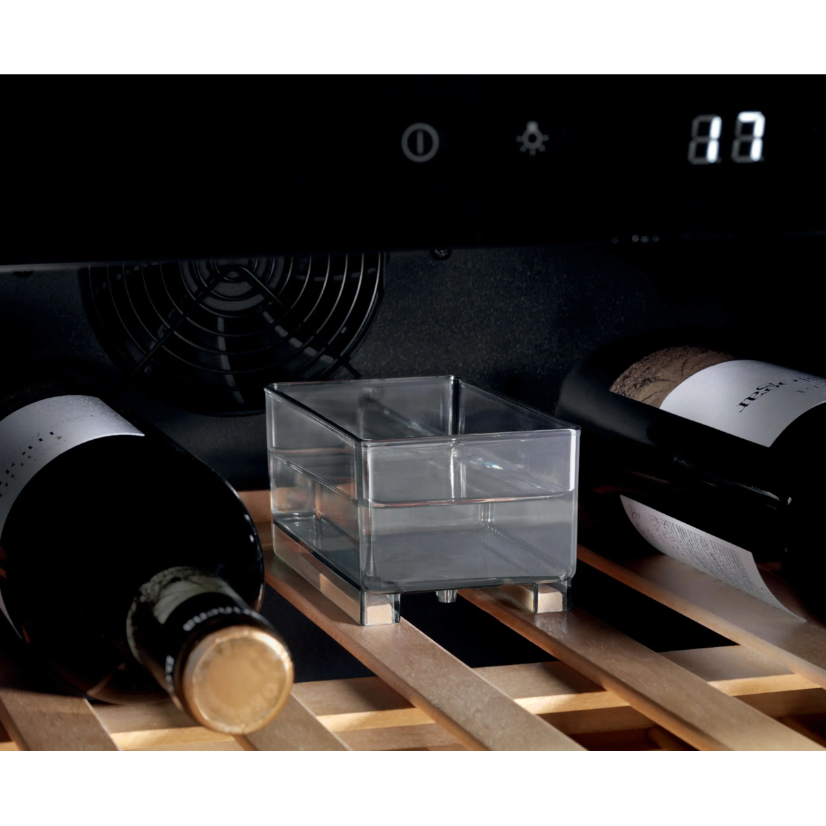 Un contenitore d'acqua trasparente si trova tra due bottiglie di vino su un ripiano in legno.