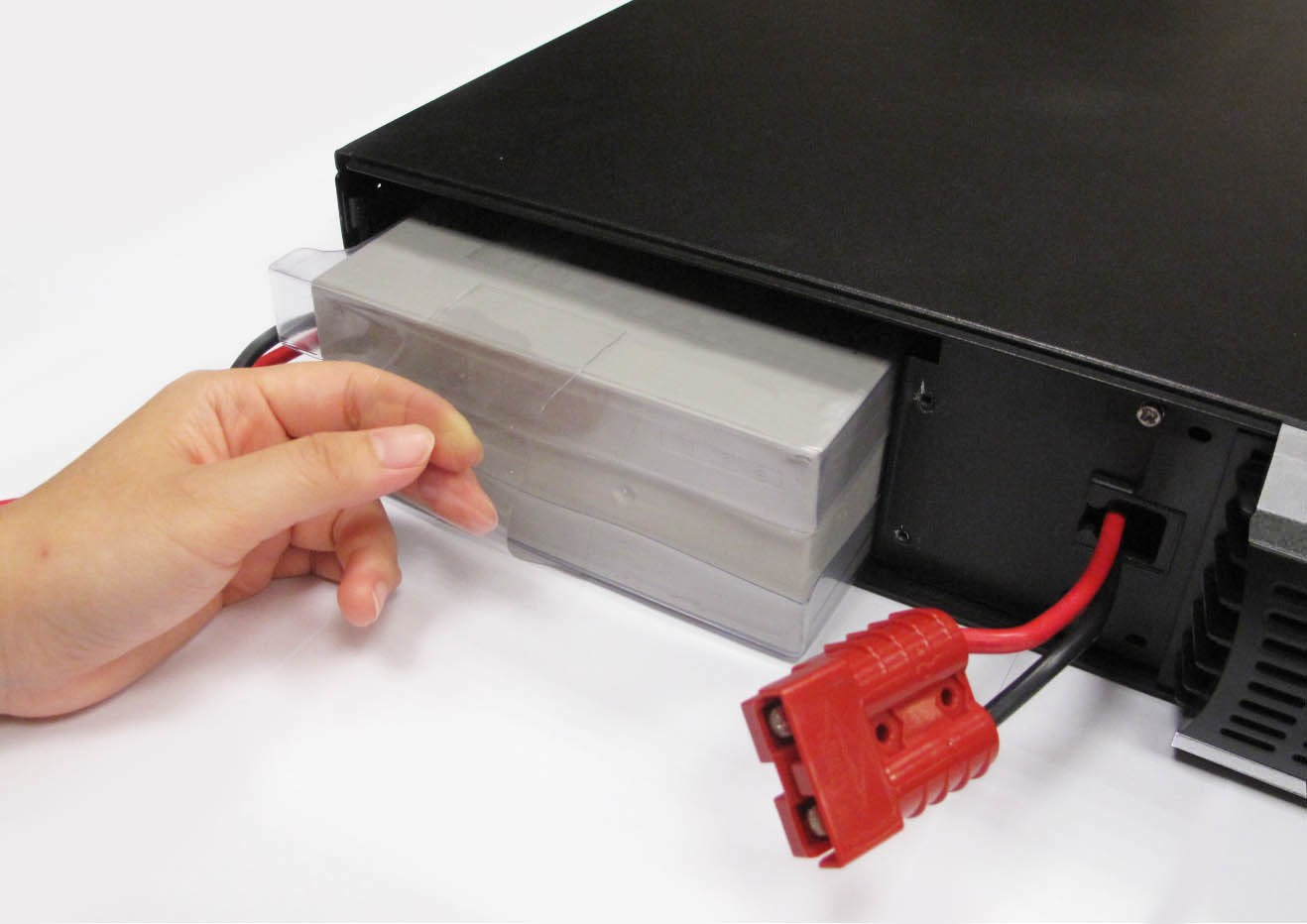 Eine Hand zieht eine Batterie aus einem schwarzen USV-Gerät, mit einem roten Anderson-Stecker im Vordergrund.