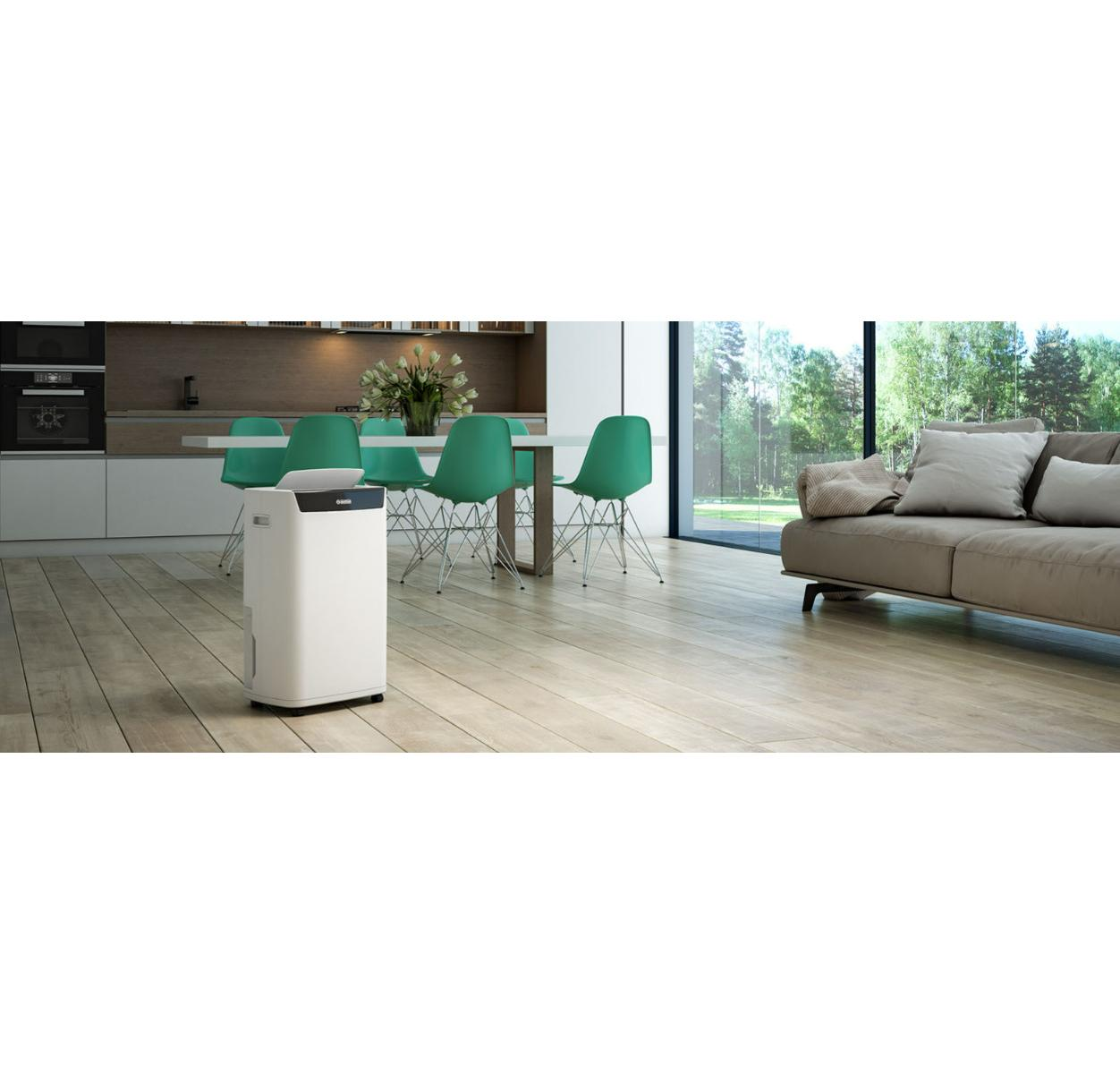 Ein weißer Luftentfeuchter steht auf Holzboden in einem modernen Wohnzimmer mit Essbereich und grauem Sofa.