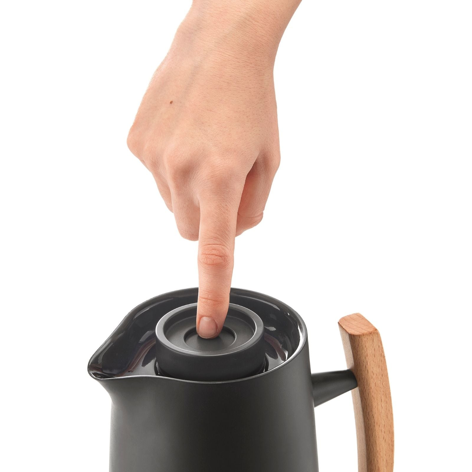 Eine Hand drückt den Deckelknopf einer schwarzen Thermoskanne mit Holzzweig auf weißem Hintergrund.