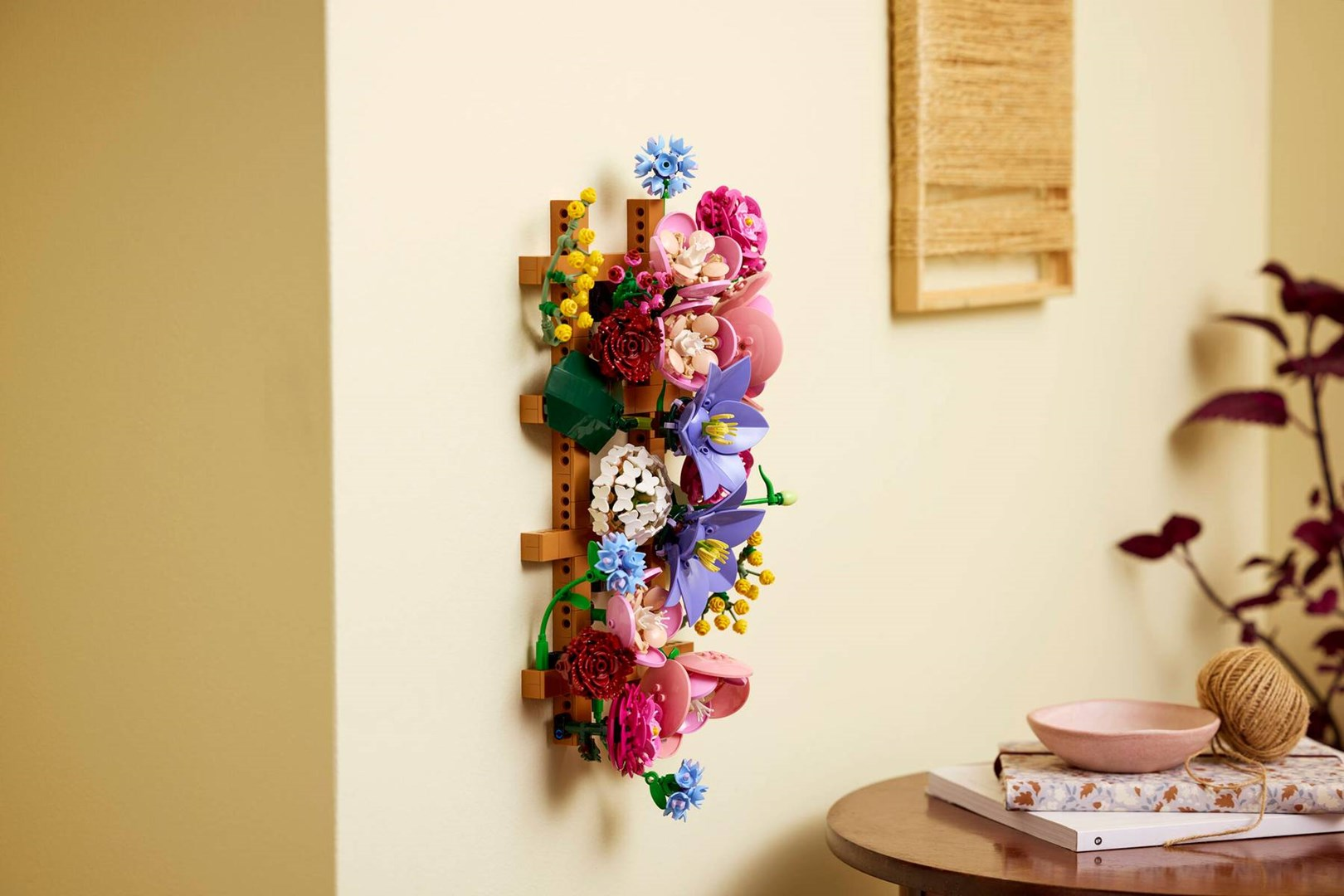 Una colorata composizione di fiori Lego è montata verticalmente su una parete chiara.