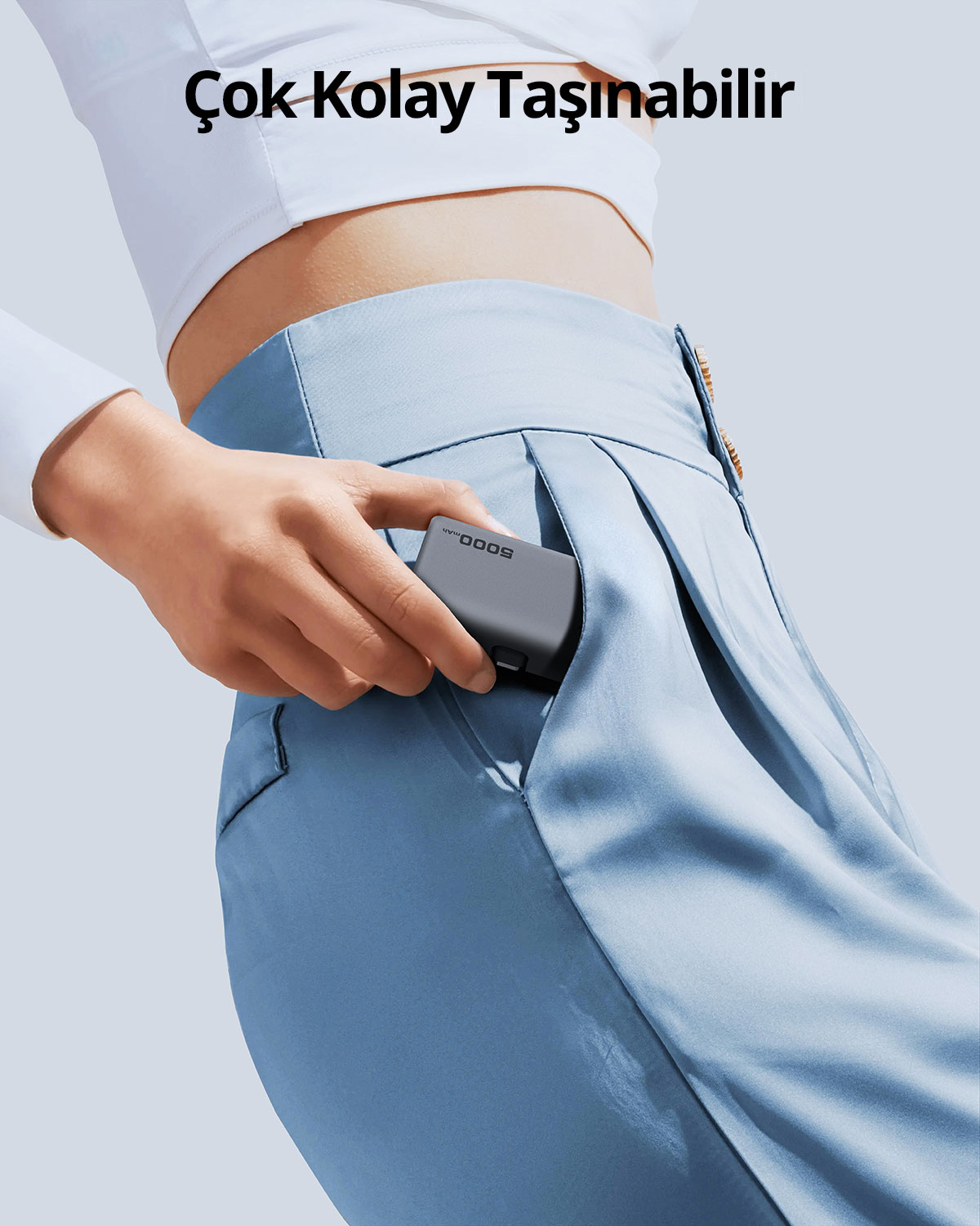 Bir el, küçük gri powerbank'i pantolon cebine koyuyor. Mavi pantolon ve beyaz üst.