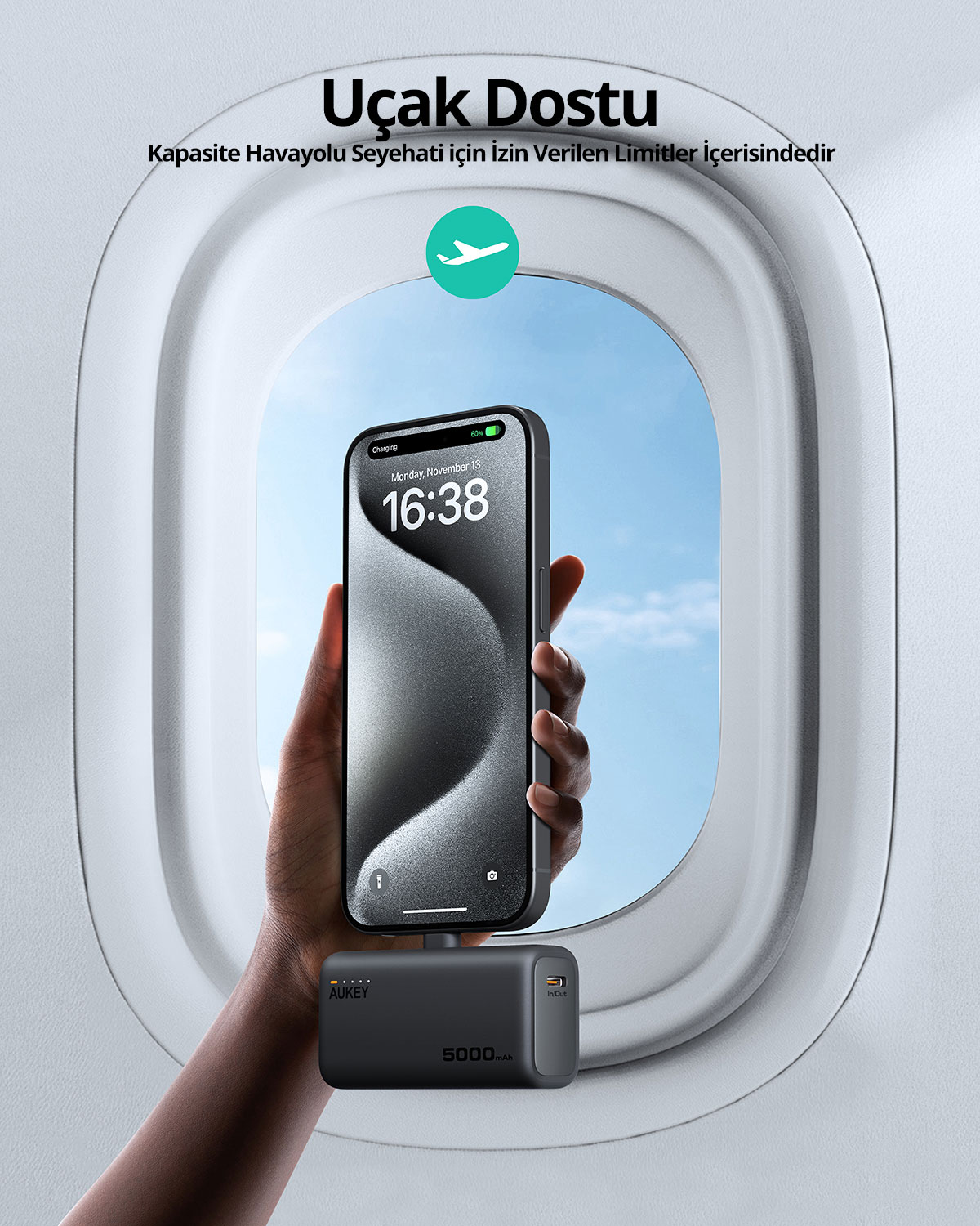 Bir el, uçak penceresinin önünde küçük siyah bir taşınabilir şarj cihazıyla şarj olan bir telefon tutuyor.