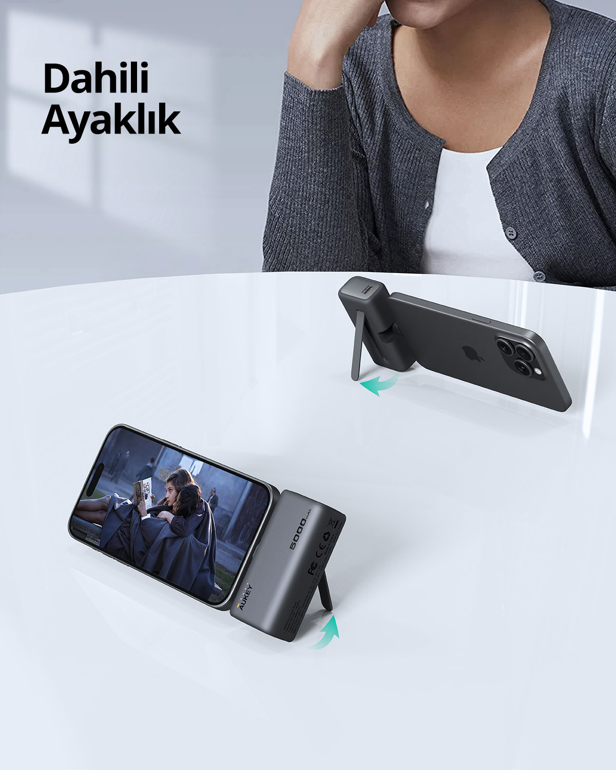 Entegre ayaklı gri bir taşınabilir şarj cihazıyla desteklenen akıllı telefon beyaz masada duruyor.