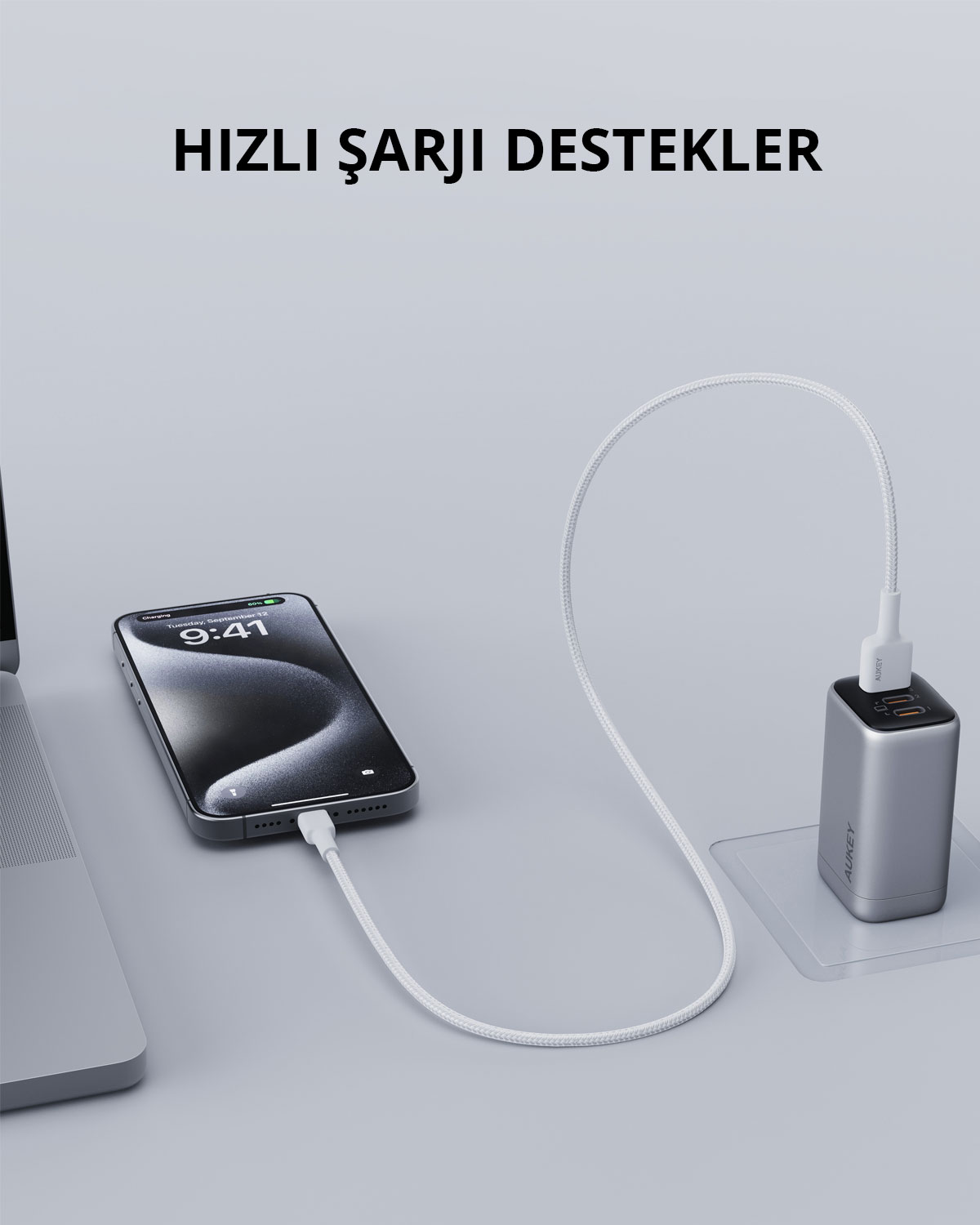 Gri bir yüzeyde beyaz kabloyla duvar şarj cihazına bağlı gümüş renkli bir akıllı telefon.