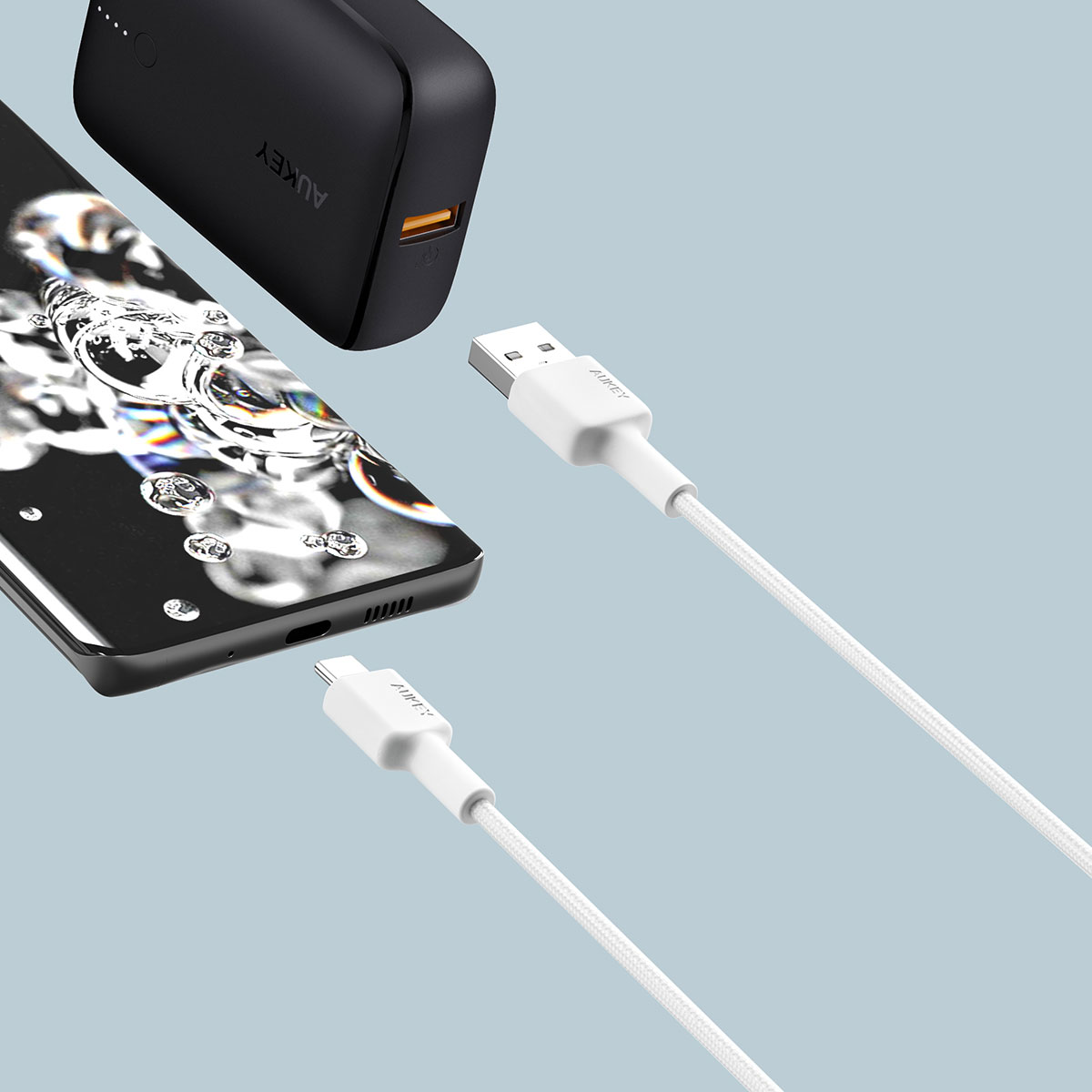 Gri arka planda siyah bir taşınabilir şarj cihazı, akıllı telefon ve beyaz USB kabloları.