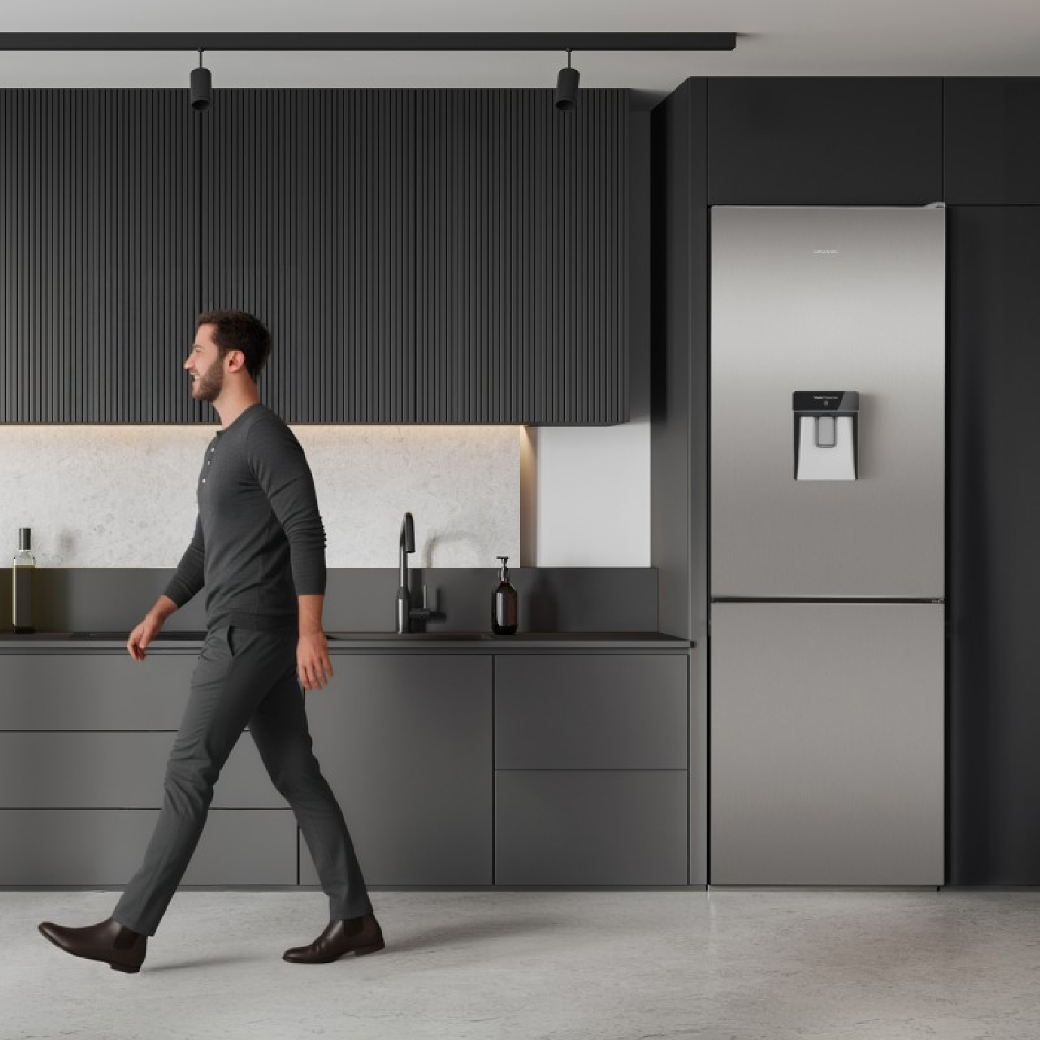 Un hombre camina por una cocina gris moderna con armarios oscuros y un refrigerador plateado.