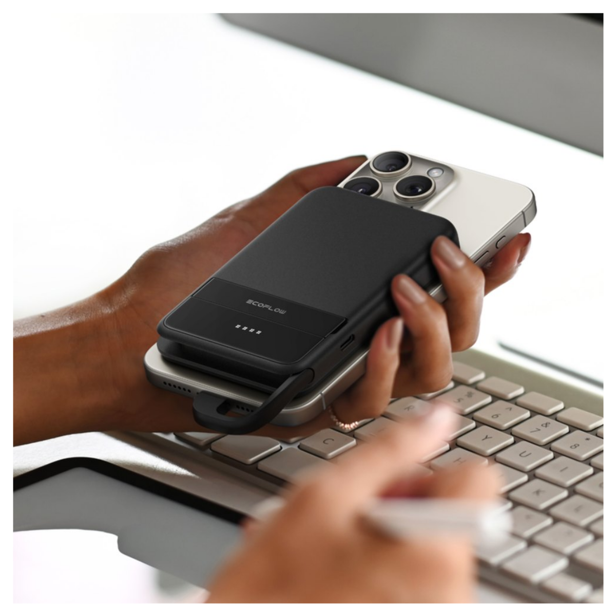 Una mano tiene uno smartphone con un power bank nero attaccato sul retro sopra una tastiera.