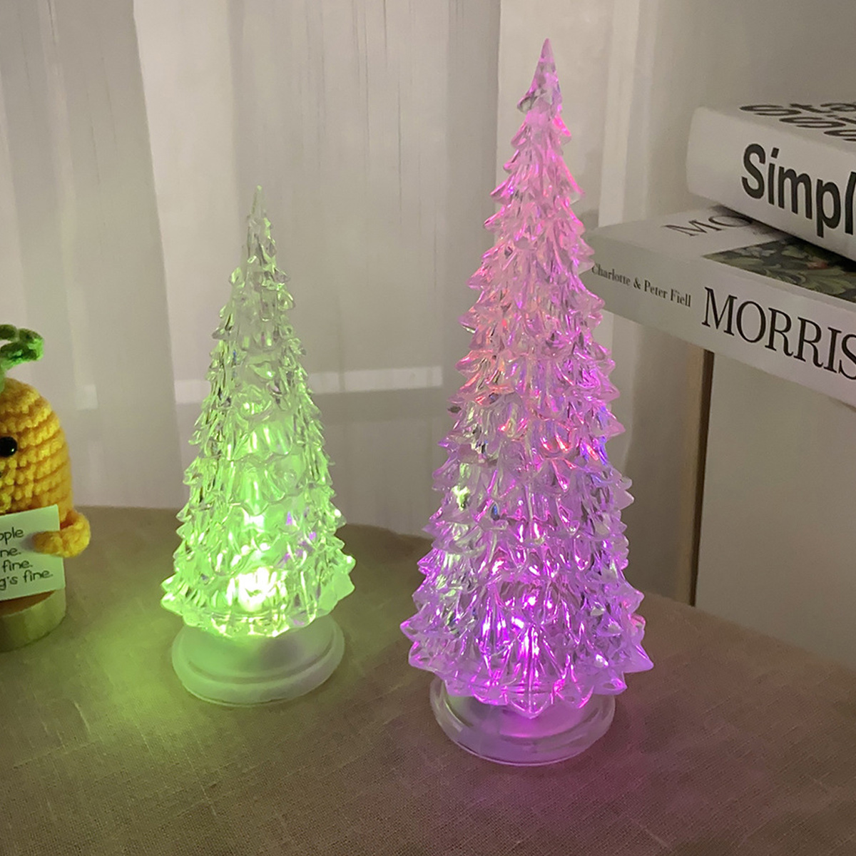 Zwei beleuchtete Acryl-Weihnachtsbäume auf einer Tischplatte, einer grün und einer pink leuchtend.