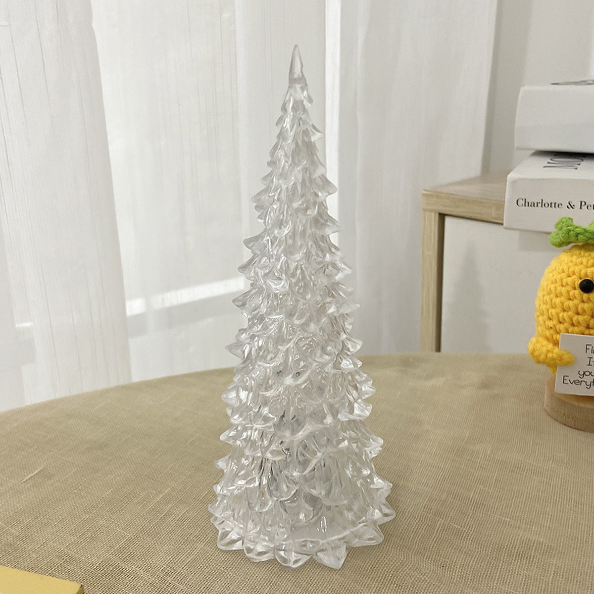 Ein glänzender, durchsichtiger Weihnachtsbaum aus Acryl steht auf einem Tisch vor hellen Vorhängen.