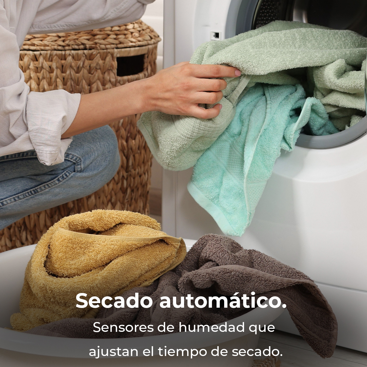 Persona sacando toallas verdes de la secadora, con un cesto de ropa amarilla y marrón delante.