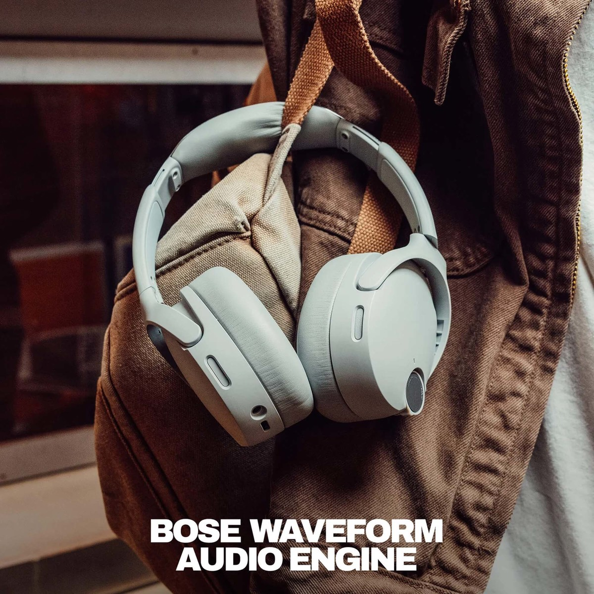 Auriculares grises de Bose colgando del bolsillo de una chaqueta y correa de mochila.