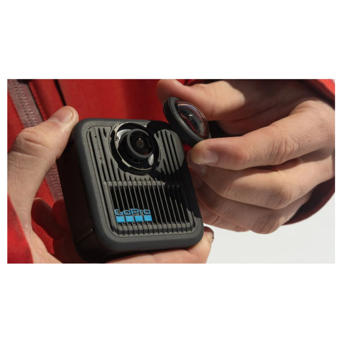 Eine Person hält eine schwarze GoPro-Kamera und entfernt oder platziert deren runden Linsenschutz.
