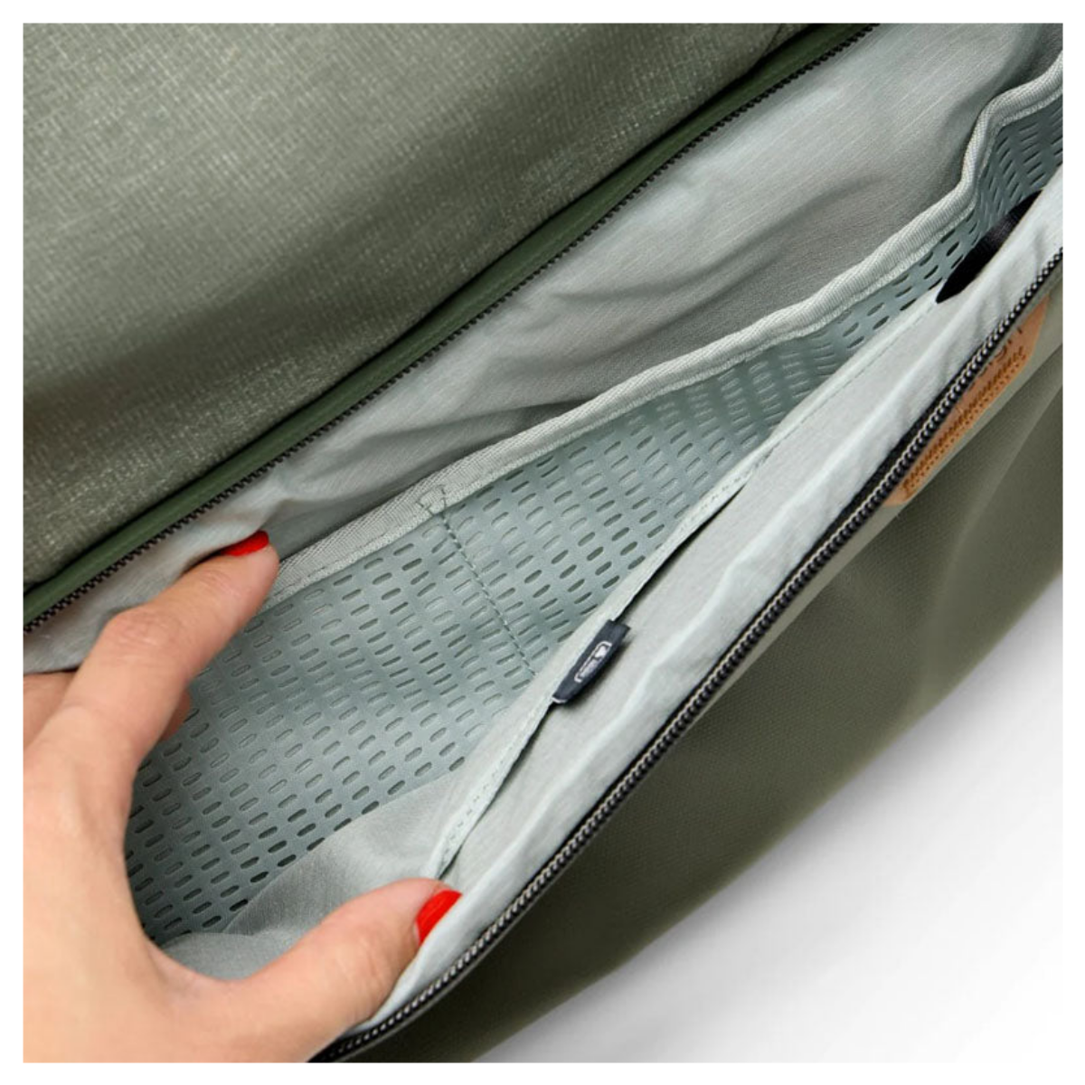 Hand öffnet das innere Fach einer grünen Tasche mit perforiertem Stoff.