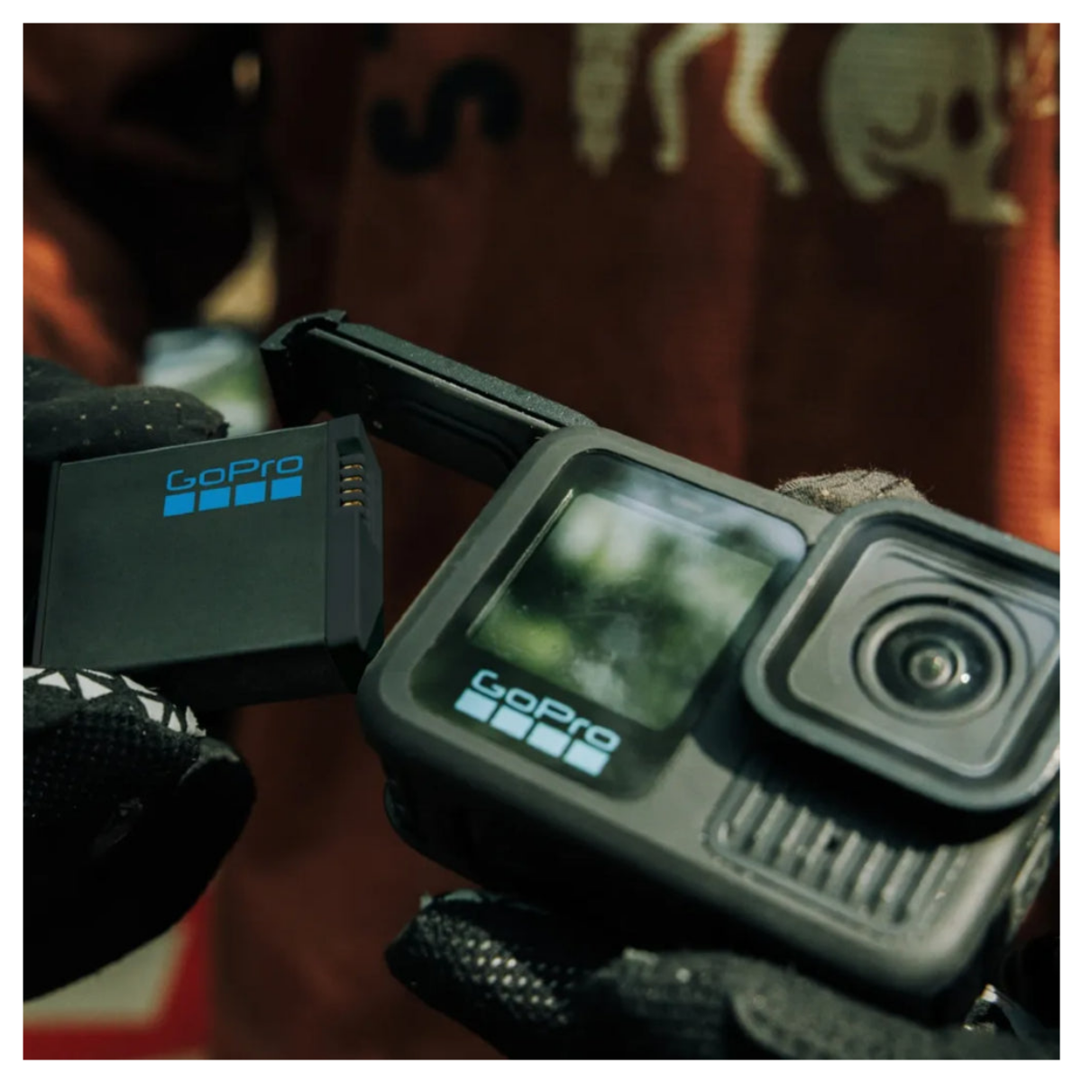 Ręka w rękawiczce wkłada baterię do otwartej kamery GoPro.