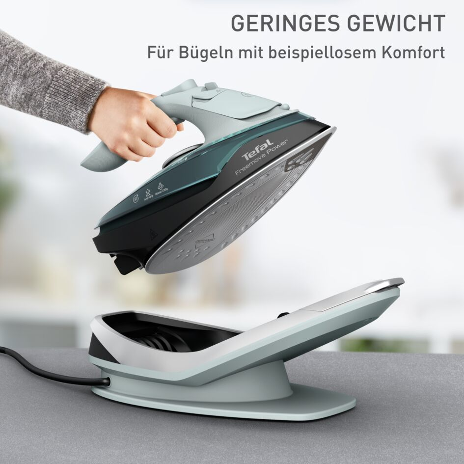 Hand hält leichtes Tefal Freemove Power Bügeleisen über seiner grauen Ladestation auf einem Tisch.