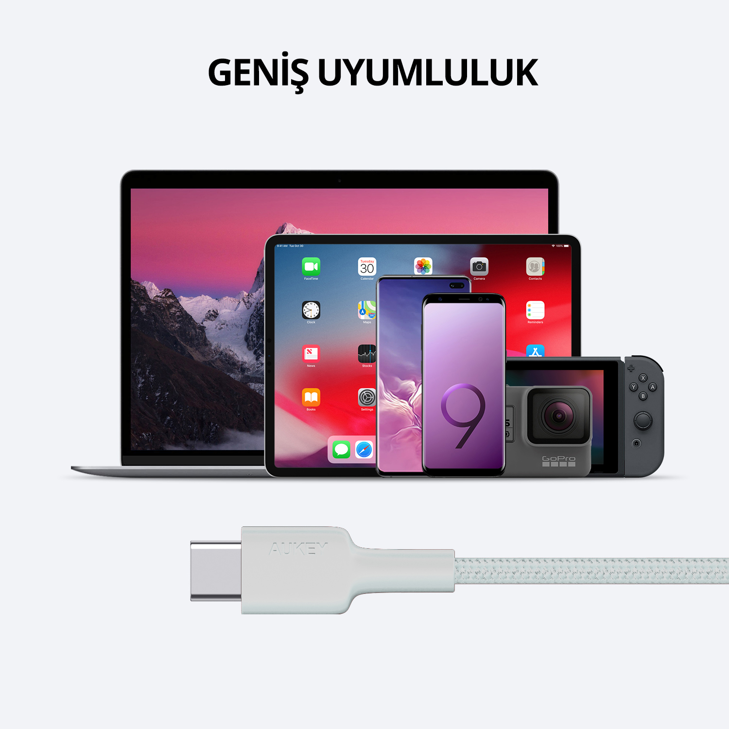 Ön planda bir USB-C kablo konnektörü ve arkasında dizüstü bilgisayar, tablet ve telefon gibi çeşitli elektronik cihazlar.