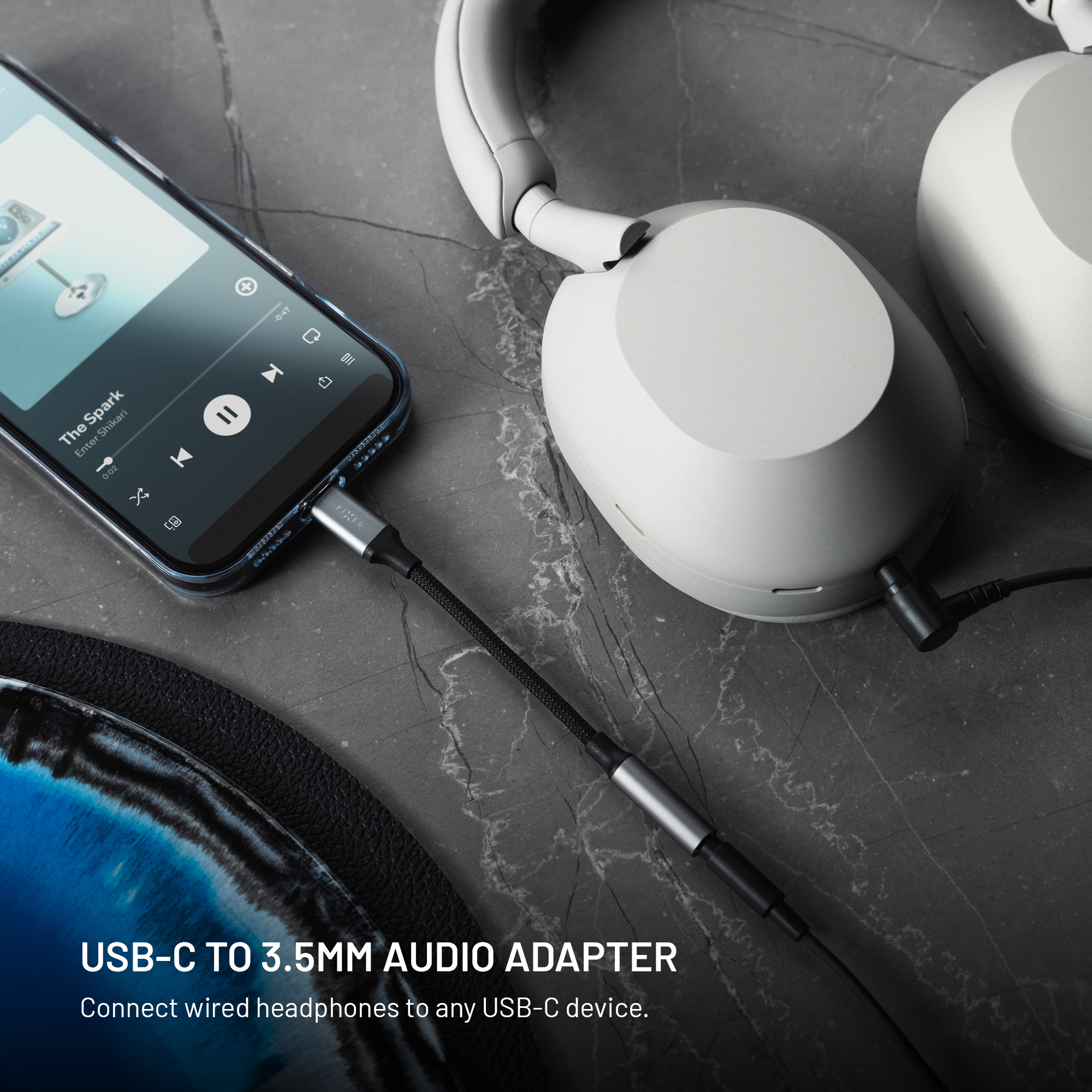Ein Smartphone und weiße Kopfhörer sind über ein USB-C-auf-3,5-mm-Audiokabel auf einer grauen Oberfläche verbunden.