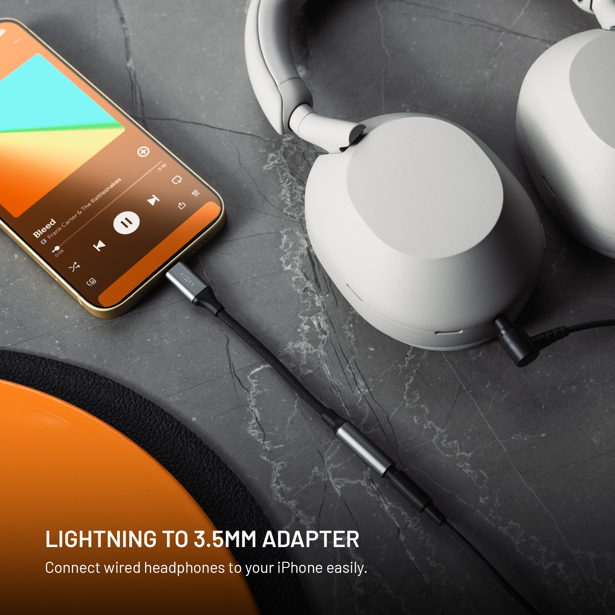 Ein Smartphone, das über einen Lightning-zu-3,5-mm-Adapter auf grauem Marmor mit weißen Kopfhörern verbunden ist.