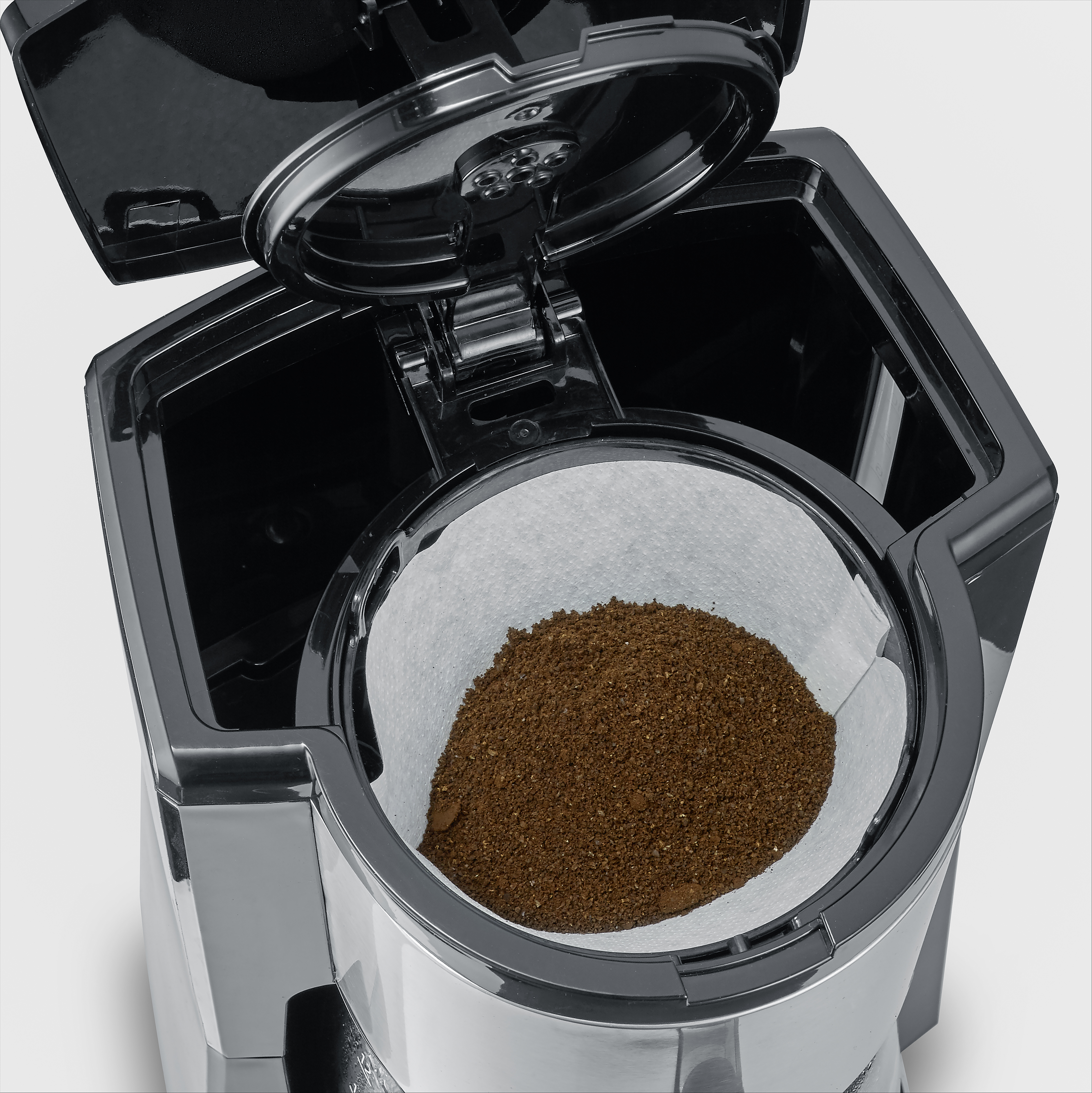 Eine offene schwarze Kaffeemaschine mit Kaffeemehl in einem weißen Papierfilter.