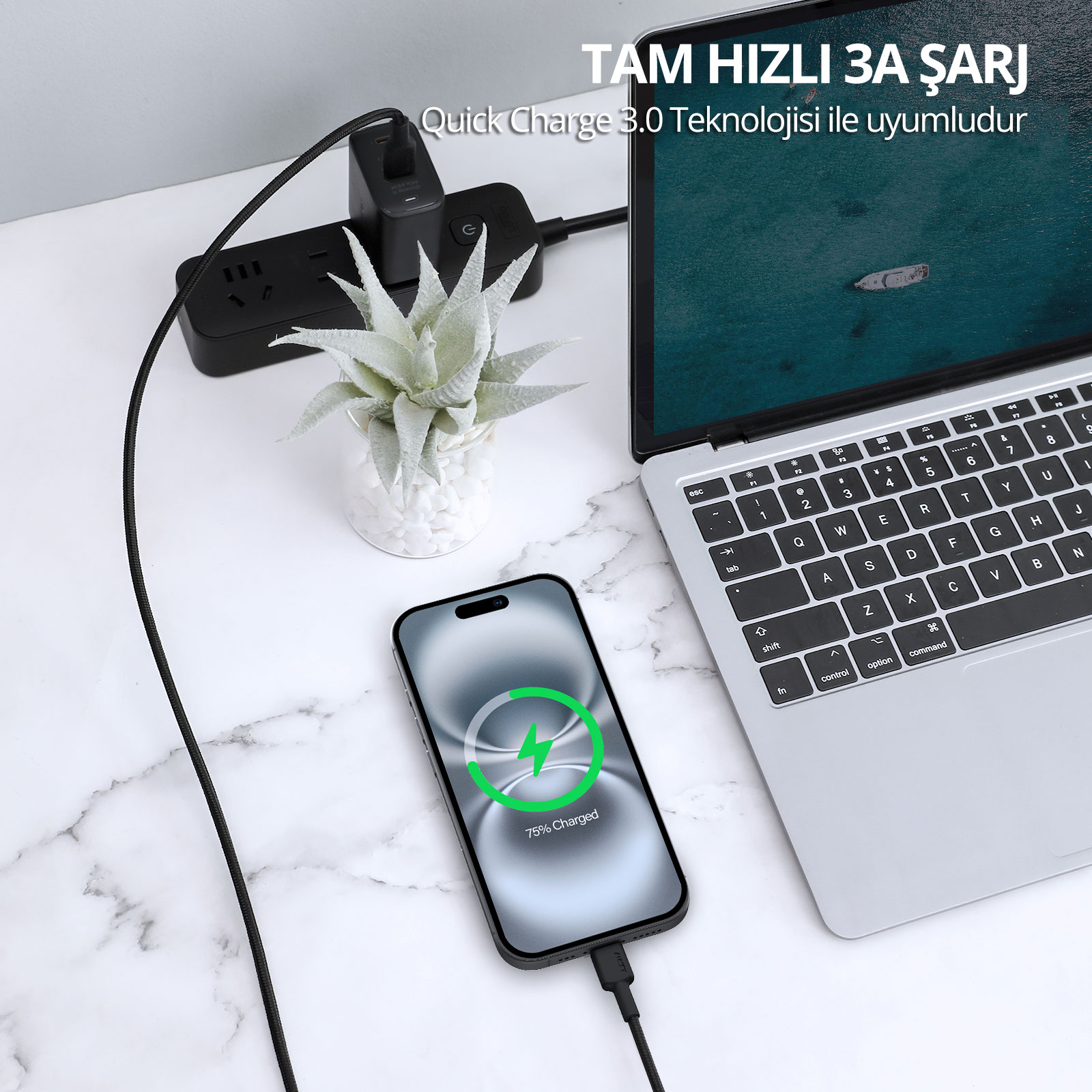 Bir akıllı telefon, dizüstü bilgisayar, bitçi ve prizin yanında bir masada kabloyla şarj oluyor.