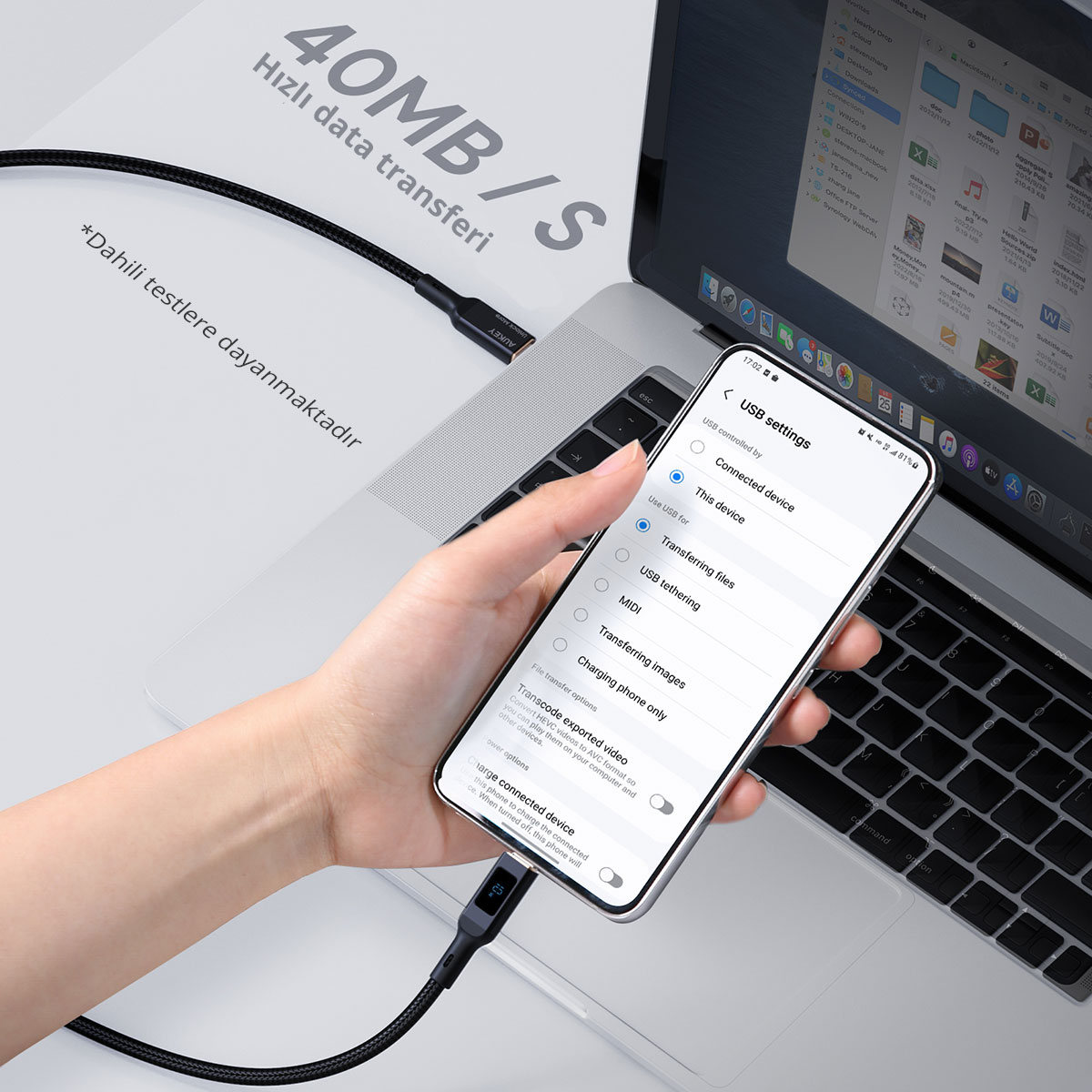 Bir elinde USB ayarları açık telefon, örgü kabloyla dizüstü bilgisayara bağlı.