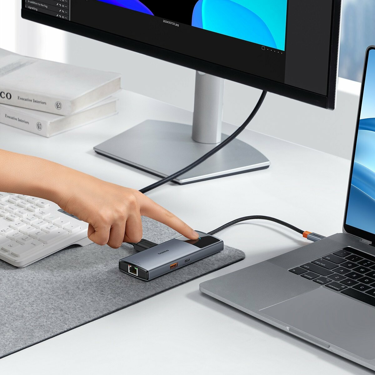 Bir el, dizüstü bilgisayar ve monitör olan bir masada USB-C hub'ına basıyor.