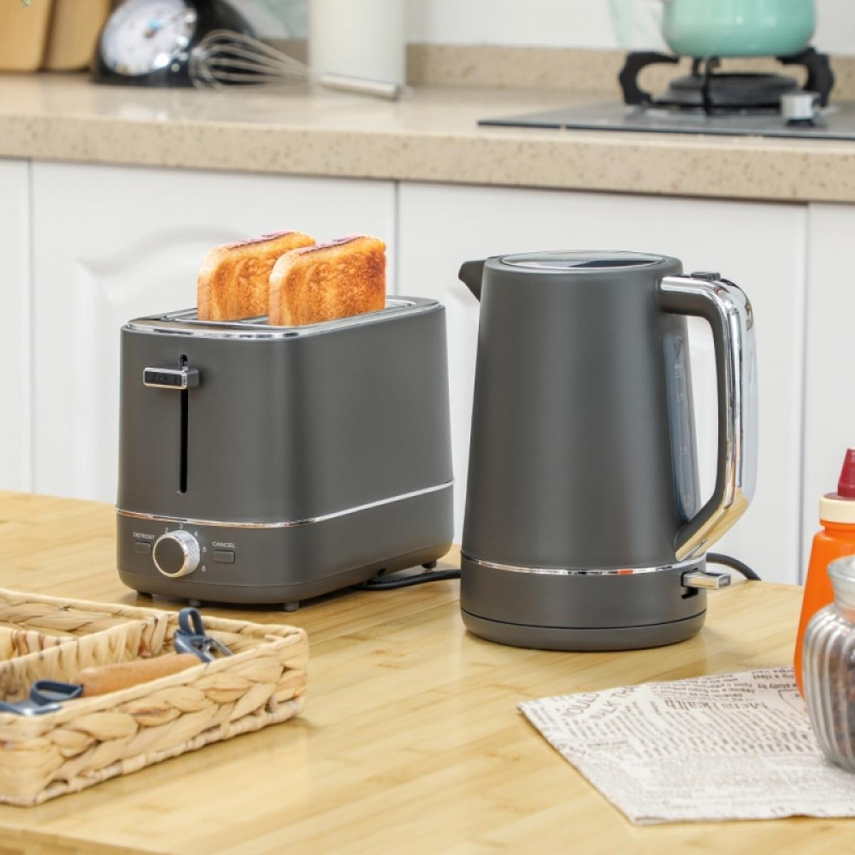 Ein dunkelgrauer Toaster mit zwei Toastscheiben und ein passender Wasserkocher stehen auf einer Holztheke.