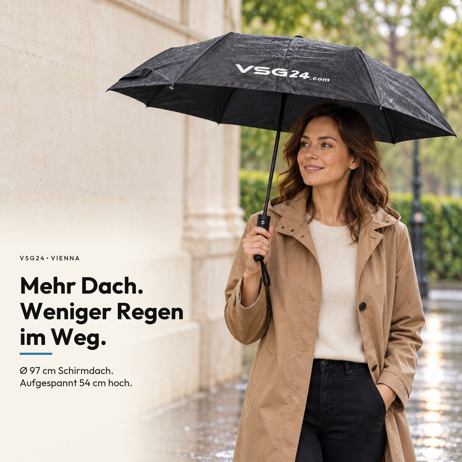 Eine Frau im Regenmantel hält einen schwarzen Regenschirm mit der Aufschrift VSG24 vor einer Steinwand.