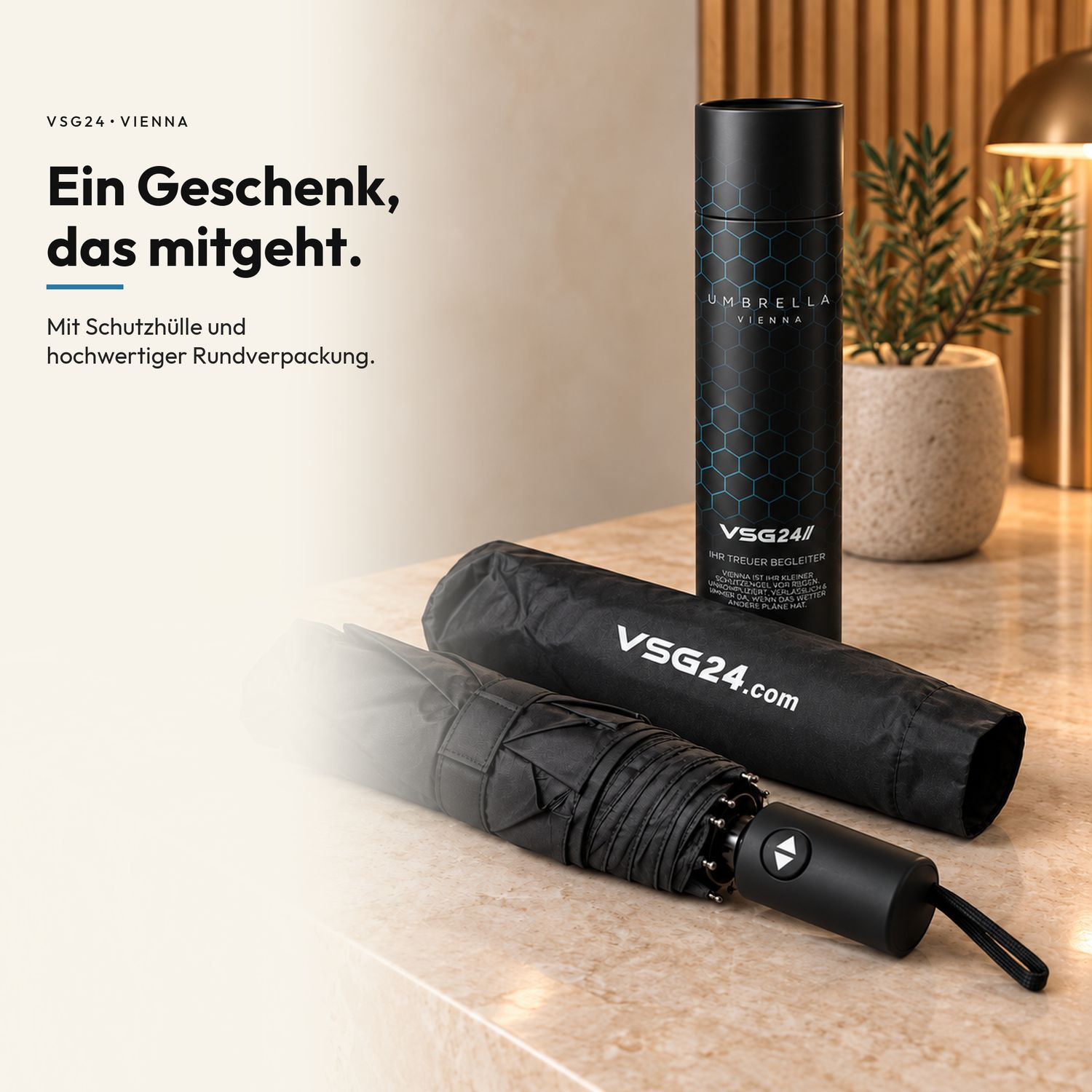 Ein schwarzer Regenschirm mit Hülle und zylindrischer Geschenkbox auf Marmor.