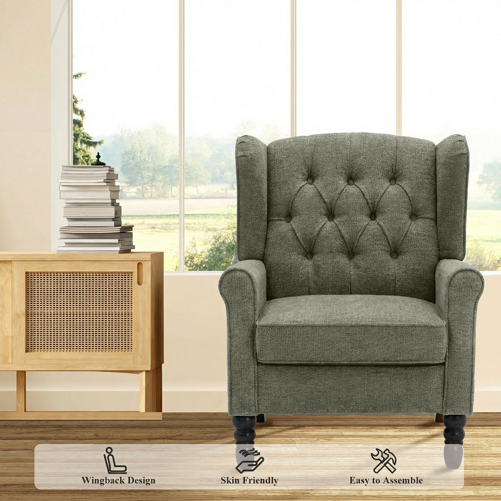 Una poltrona orecchiona grigia capitonnè davanti a una grande finestra, vicino a un mobile in legno con libri.