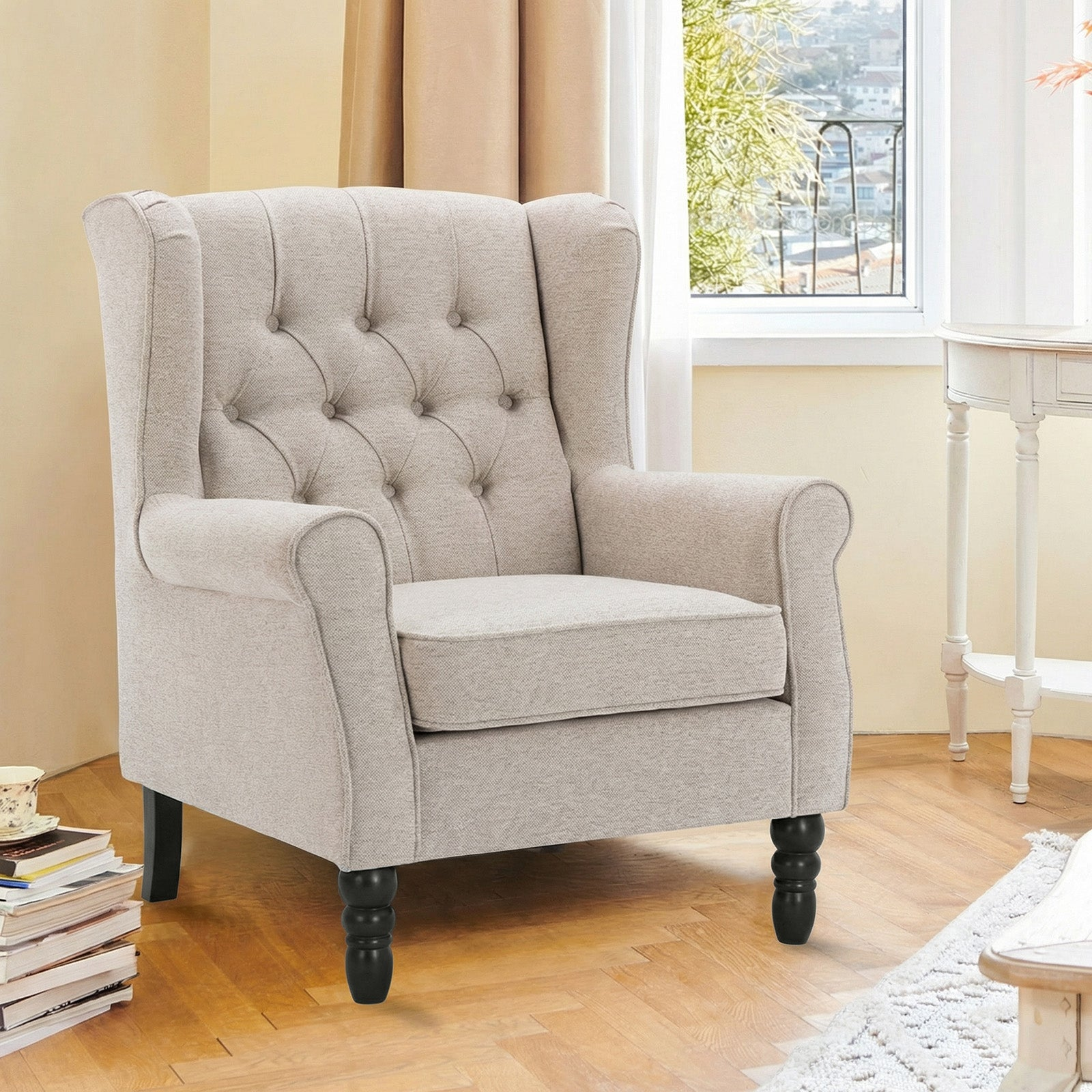 Una poltrona orecchiona beige trapuntata con gambe in legno scuro in una stanza luminosa.