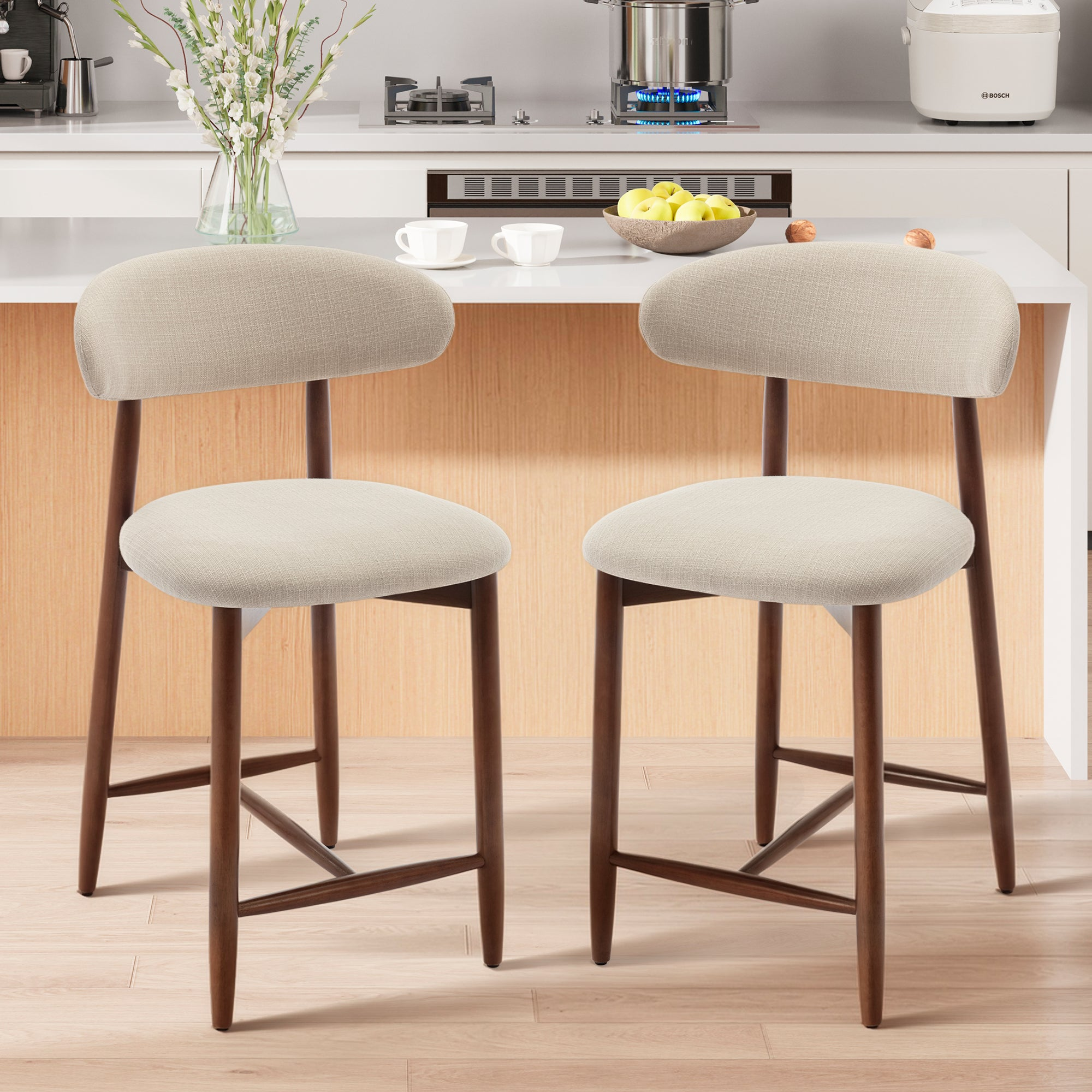 Due moderni sgabelli da bar con rivestimento beige e gambe in legno scuro davanti a un bancone da cucina bianco.