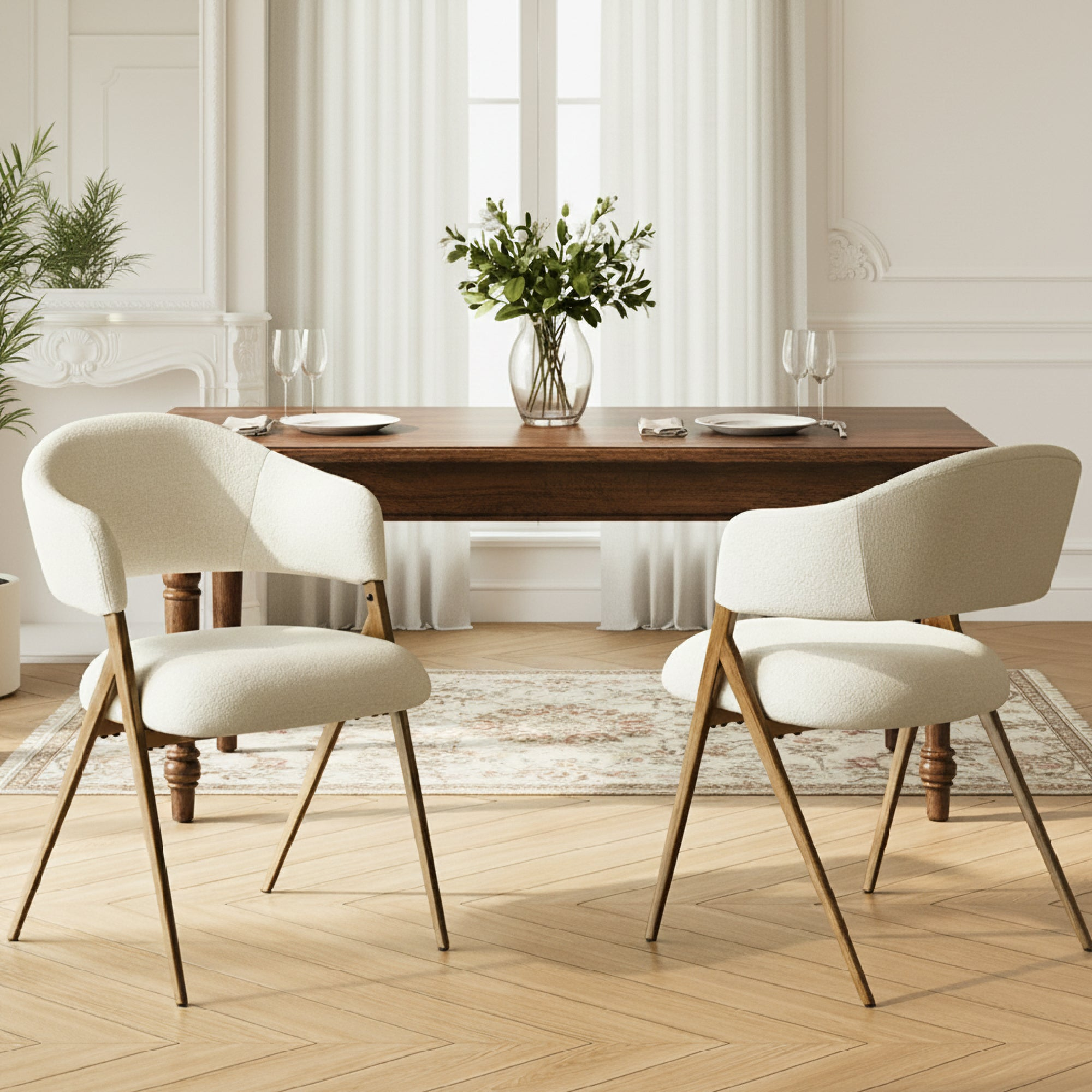 Due poltroncine bianche davanti a un tavolo da pranzo in legno con vaso e coperti in una stanza luminosa.