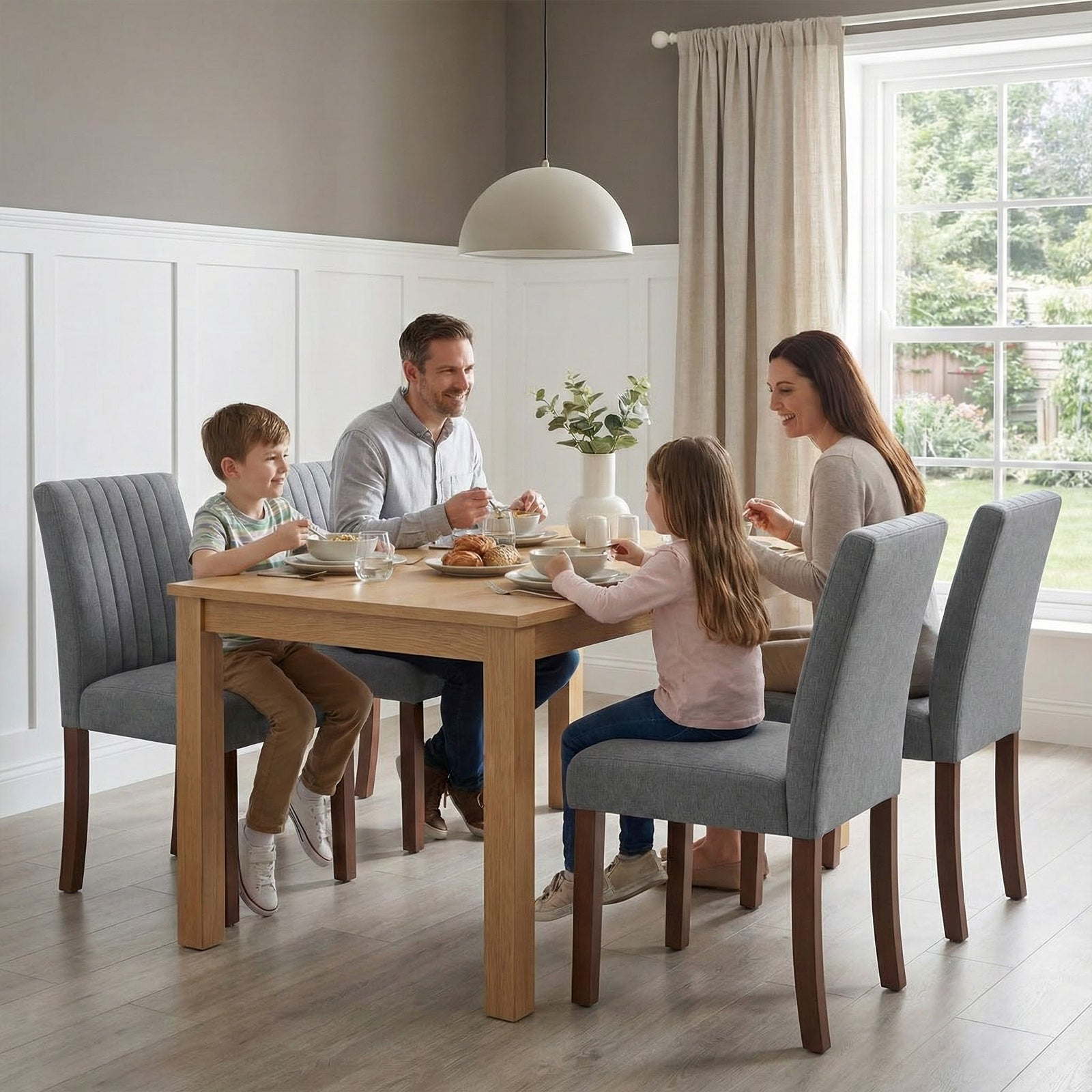 Una famiglia di quattro persone fa colazione insieme a un tavolo di legno in una sala da pranzo.