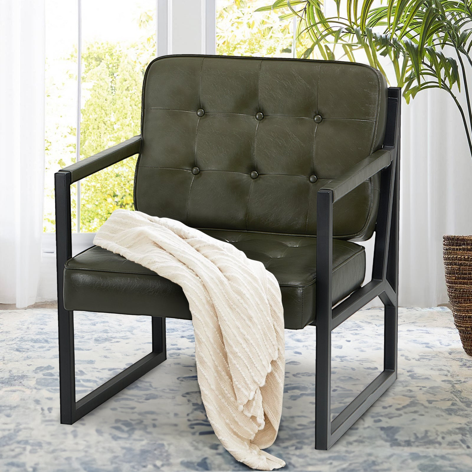 Poltrona verde con struttura in metallo nero, bottoni trapuntati e una coperta chiara.