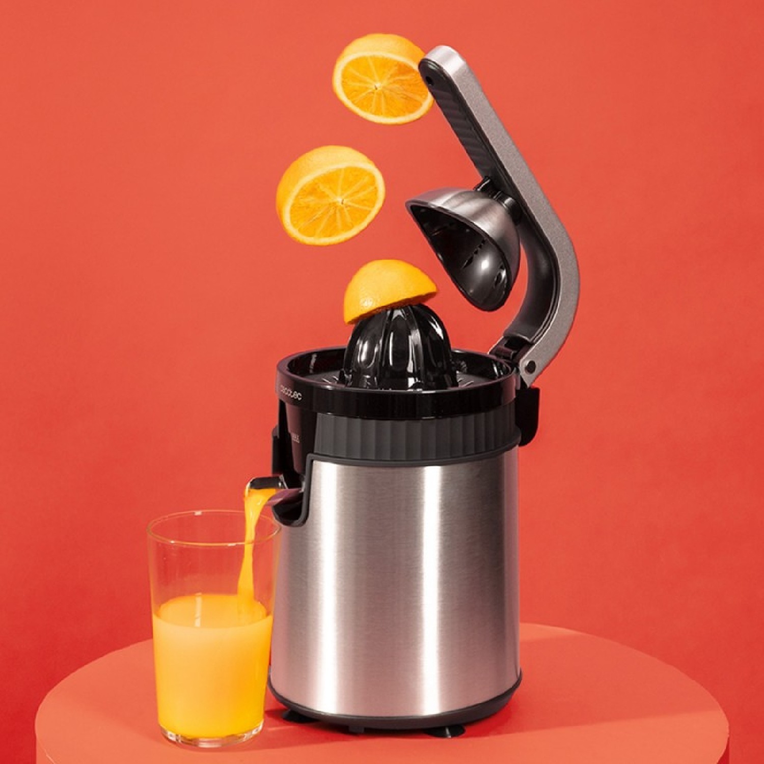 Eine Edelstahl-Zitruspresse presst Orangen auf rotem Hintergrund, Saft fließt in ein Glas.