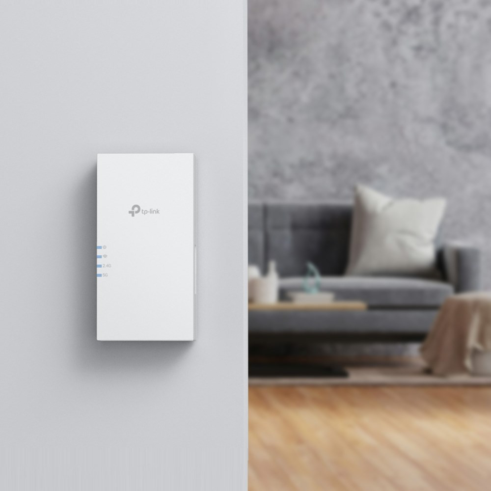 Biały wzmacniacz sygnału Wi-Fi TP-Link na ścianie na tle rozmytego salonu.