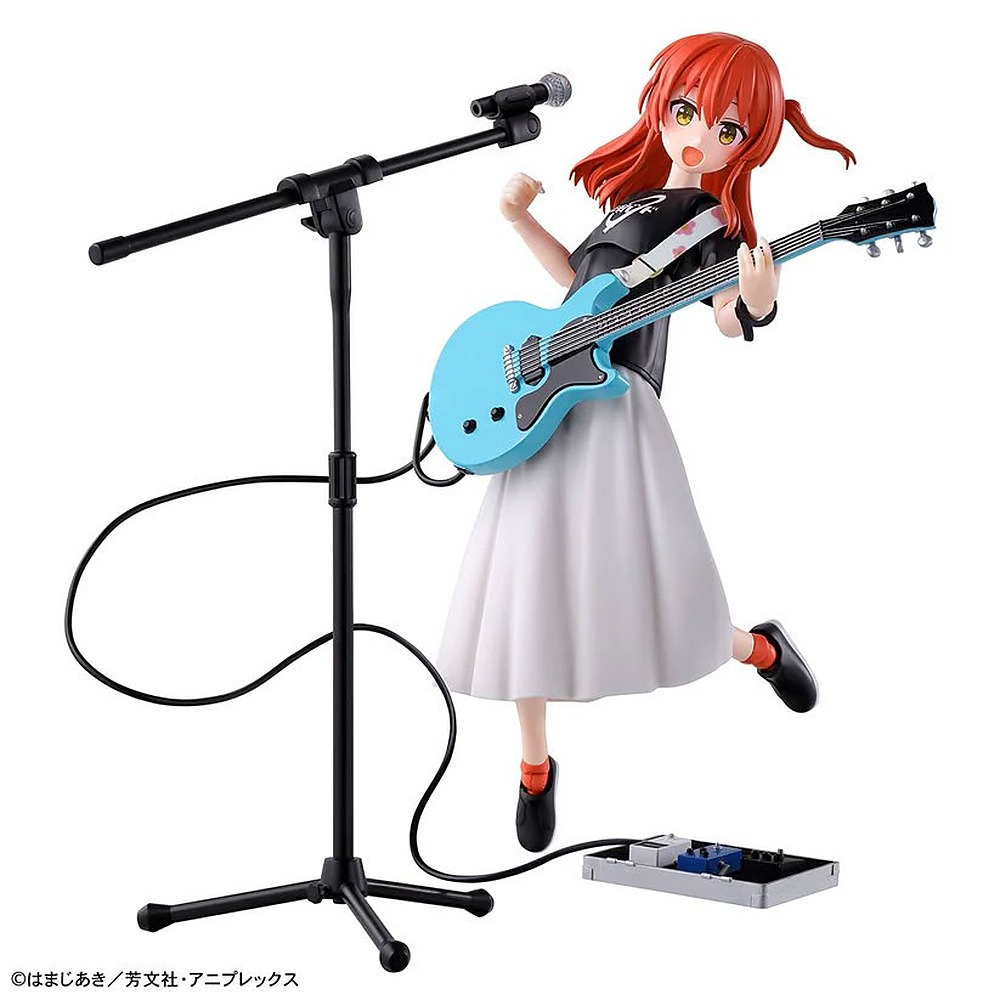 Figura anime z rudymi włosami śpiewa do mikrofonu i gra na jasnoniebieskiej gitarze elektrycznej obok statywu.