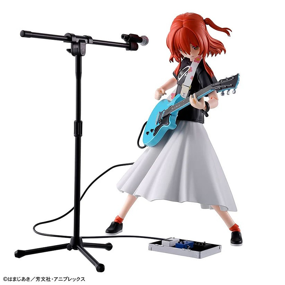 Figura anime z rudymi włosami gra na niebieskiej gitarze elektrycznej obok statywu mikrofonowego na białym tle.