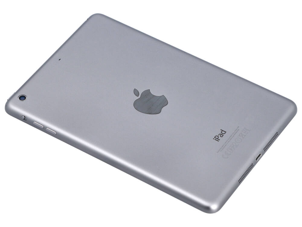 Srebrny iPad leży ukośnie na białym tle, ukazując logo Apple, aparat, przyciski oraz port ładowania.