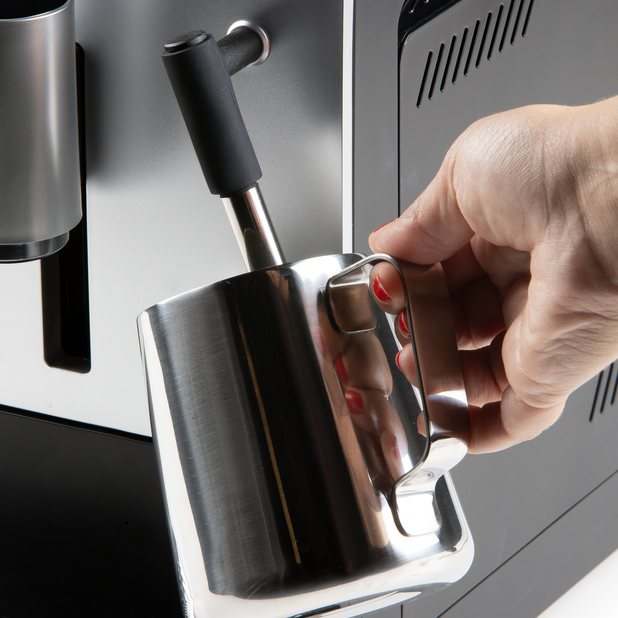 Een hand houdt een roestvrijstalen kan onder het stoompijpje van een koffiemachine.