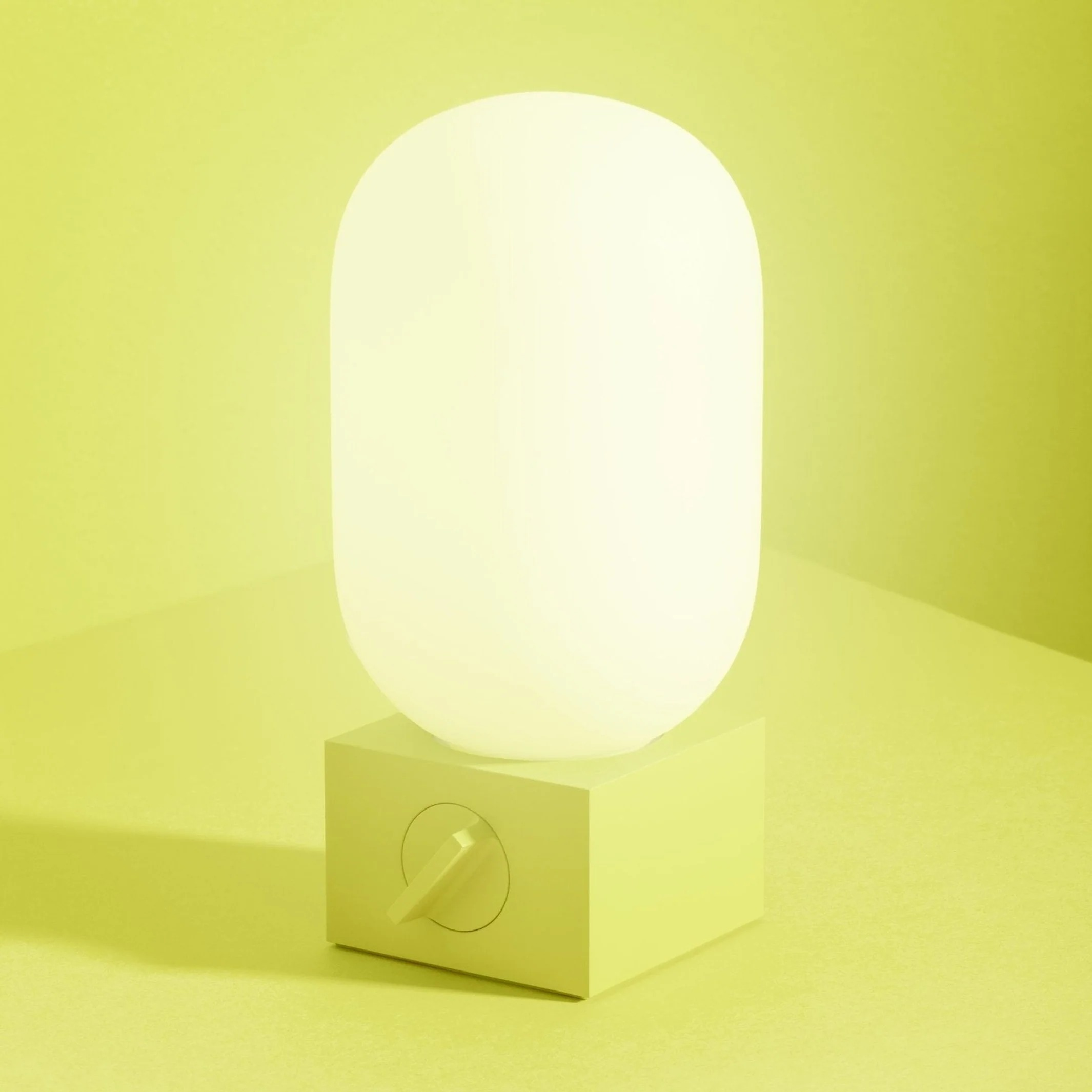 Zielona lampa z owalnym bia łym kloszem stoi na zielonej powierzchni pod zieloną ścianą.